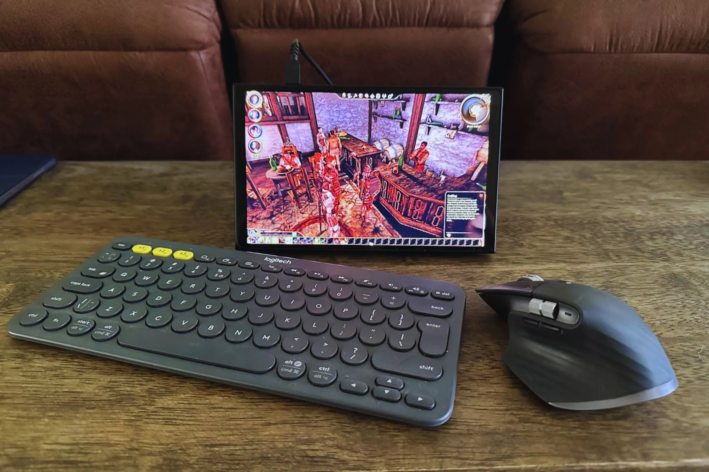 Bàn phím Logitech K380 màu đen và chuột MX Master 3S cùng thiết bị Lenovo Legion Go trên bàn gỗ.