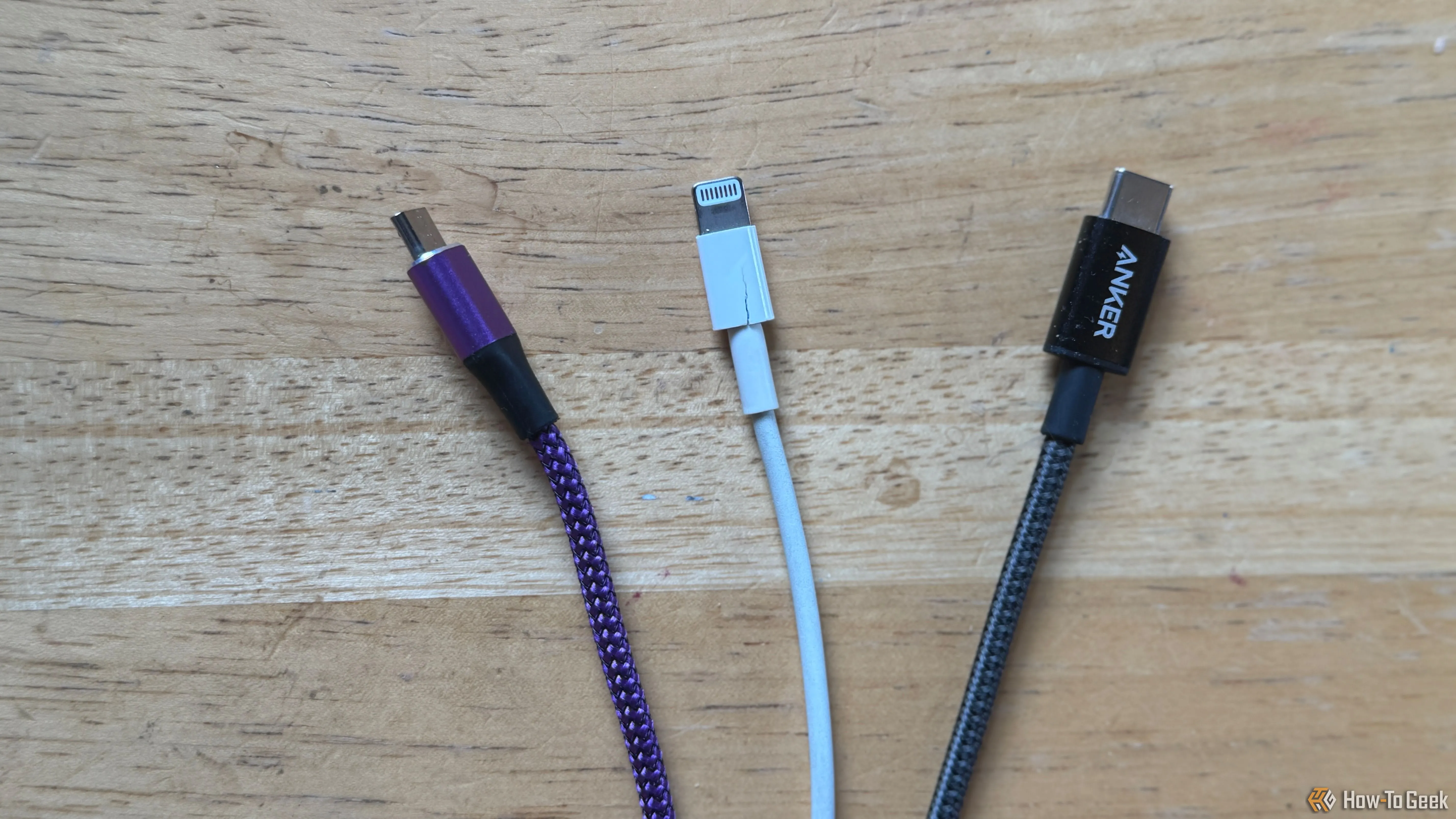 Một cáp Micro-USB màu tím, một cáp Lightning màu trắng và một cáp USB-C màu xám trên mặt bàn, minh họa cách phân loại cáp theo màu sắc.
