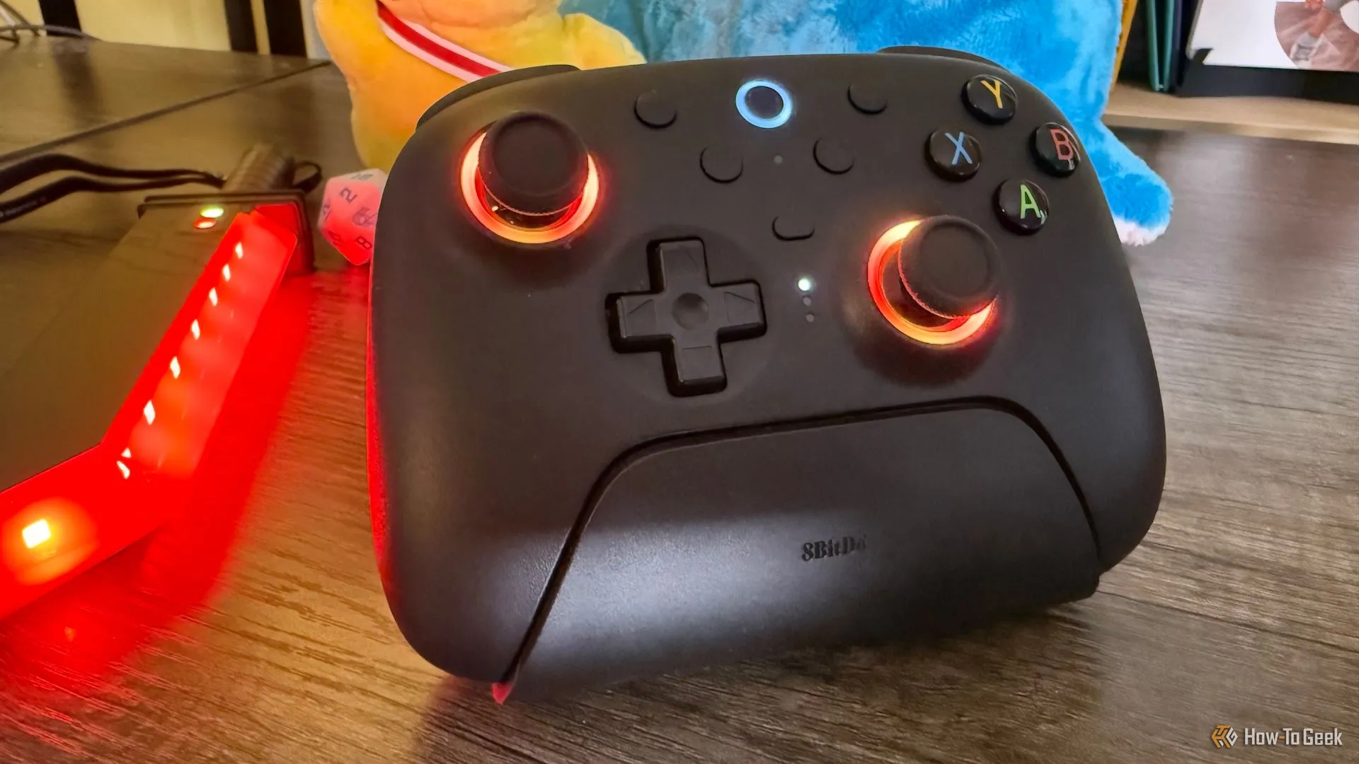 Tay cầm 8BitDo Ultimate 2 Wireless với vòng đèn RGB quanh joystick màu đỏ, hiển thị tính năng ánh sáng.