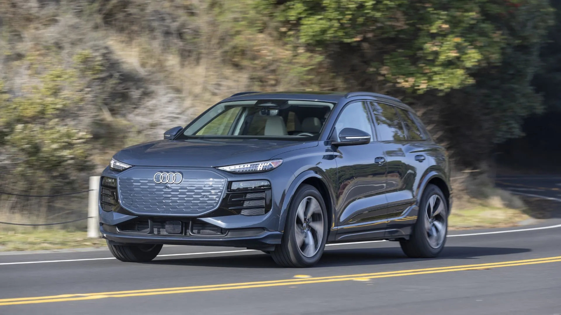 Audi Q6 e-tron 2025 màu xám đang di chuyển trên con đường nông thôn, thể hiện sự cân bằng giữa sang trọng và hiệu suất điện