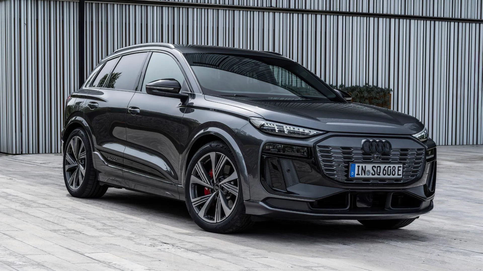 Audi SQ6 e-tron 2025 màu xám Daytona đỗ trước một tòa nhà kiến trúc hiện đại, nhấn mạnh thiết kế điện khí và hiệu suất