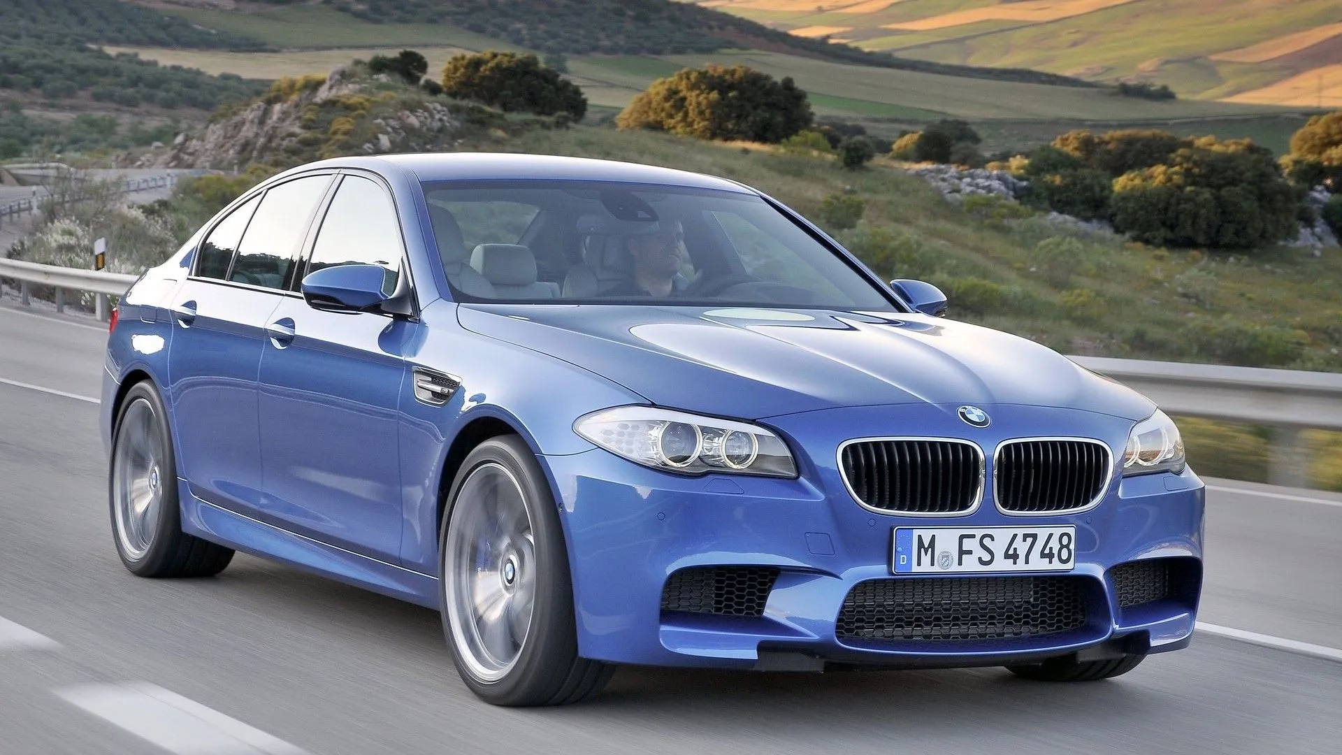 BMW M5 F10 2013 màu xanh dương thể thao đang di chuyển trên đường, thể hiện sức mạnh vượt trội
