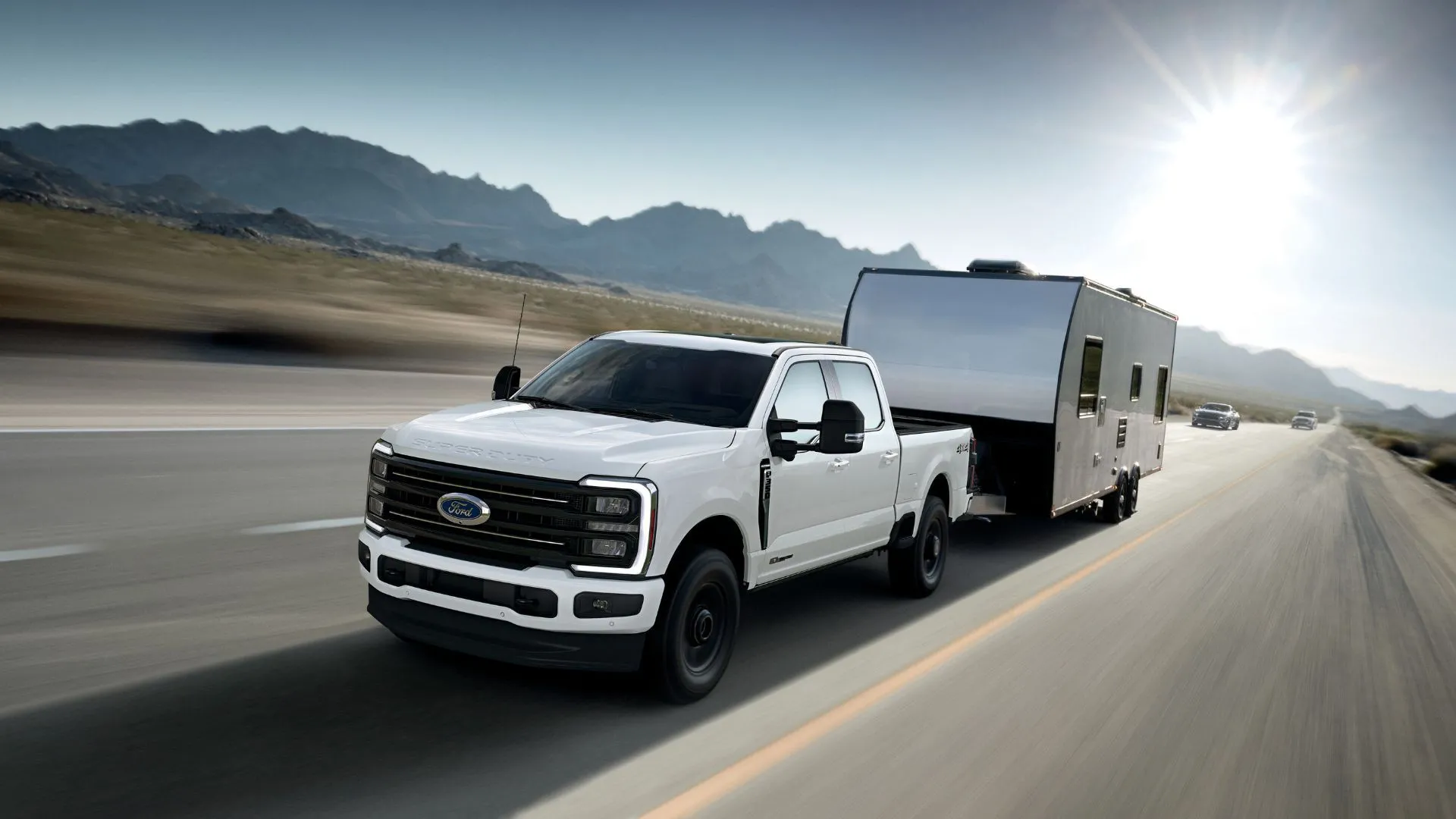Cận cảnh mặt trước 3/4 của chiếc Ford F-350 Super Duty Platinum 2025 màu trắng đang kéo rơ moóc với núi ở hậu cảnh.
