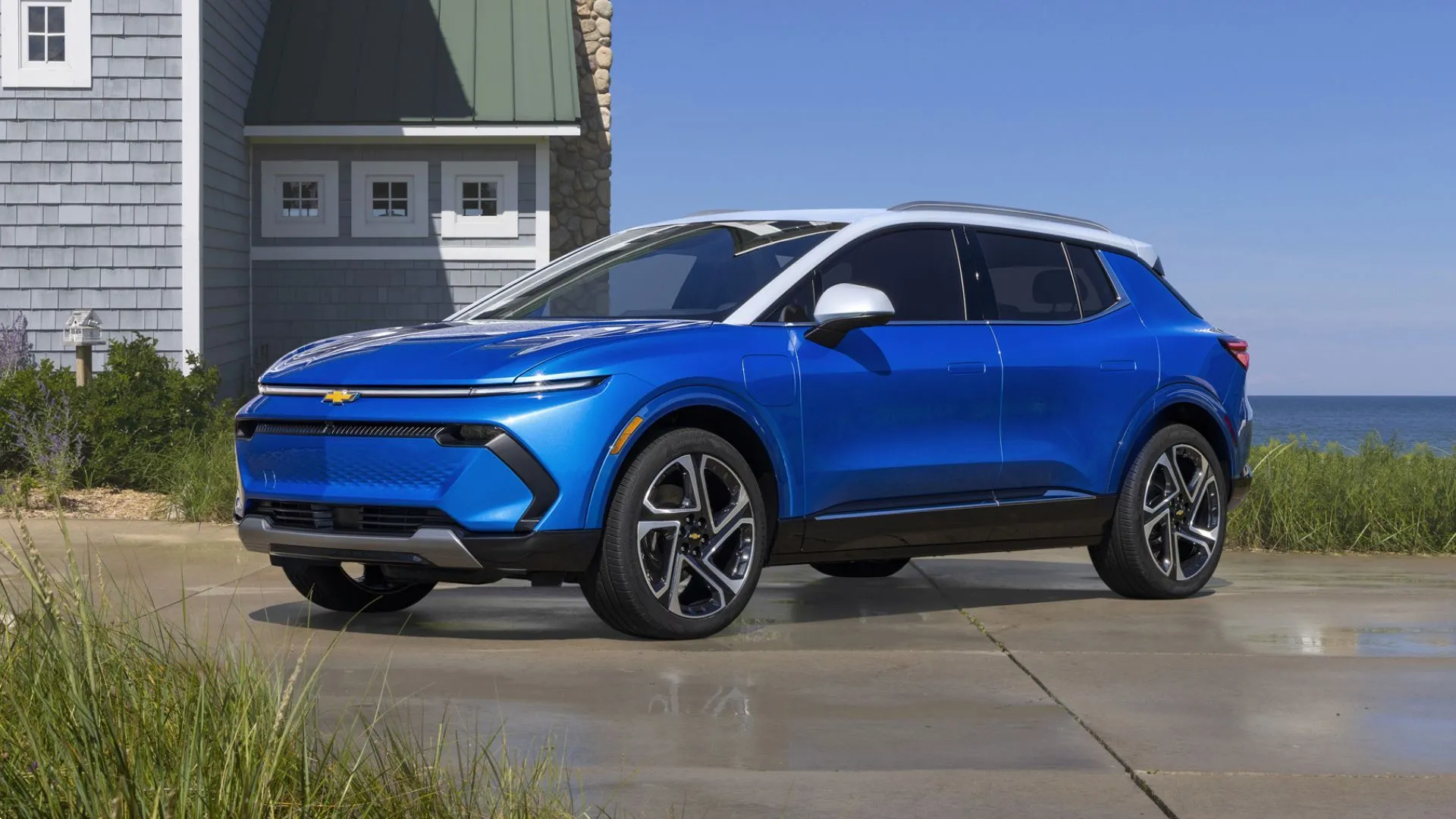 Chevrolet Equinox EV 2025 màu xanh dương, góc 3/4 phía trước, đỗ bên ngoài ngôi nhà ven biển, minh họa mẫu crossover điện.