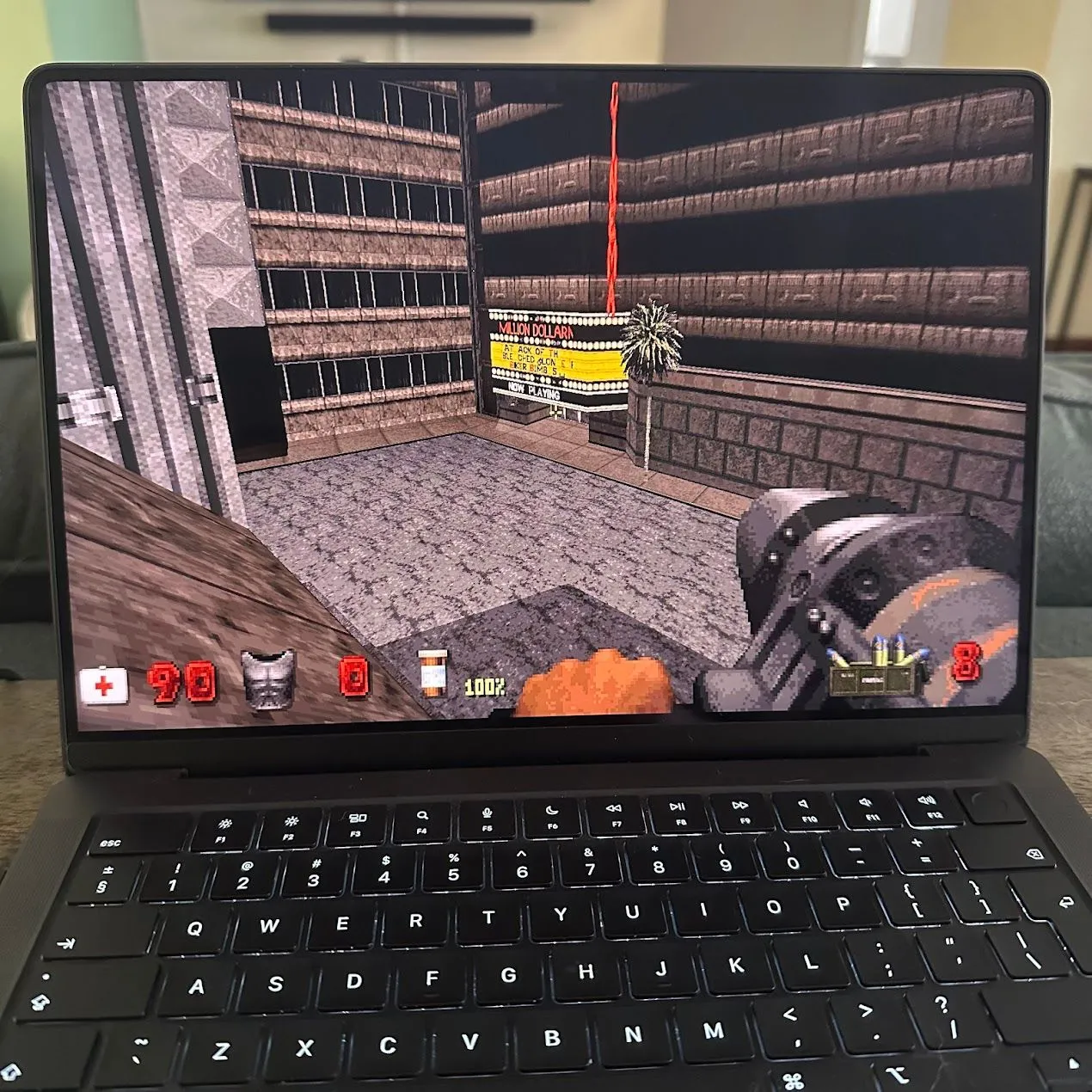 Duke Nukem 3D đang chạy trên MacBook Pro, hiển thị cảnh chiến đấu từ góc nhìn thứ nhất trong môi trường đô thị bị phá hủy với nhân vật chính đang bắn kẻ thù.