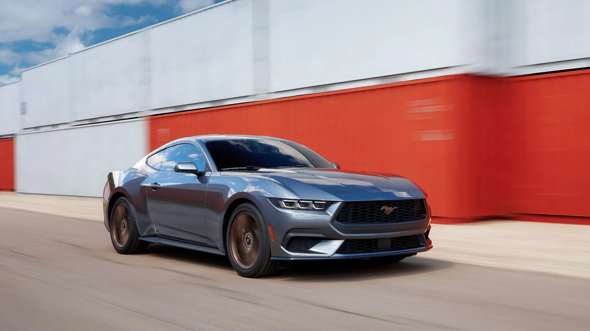 Ford Mustang 2024 màu xám bạc, dòng xe cơ bắp số sàn, đang lái qua container