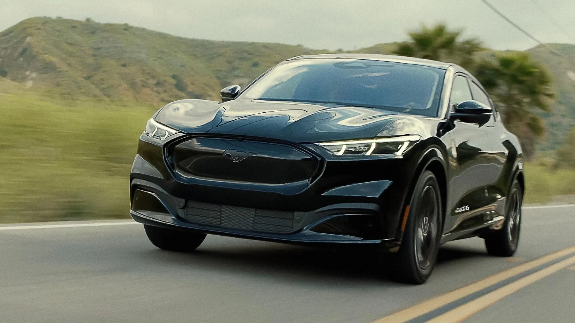 Ford Mustang Mach-E Premium 2023 màu đen đang di chuyển trên con đường nông thôn, với góc 3/4 phía trước động thái