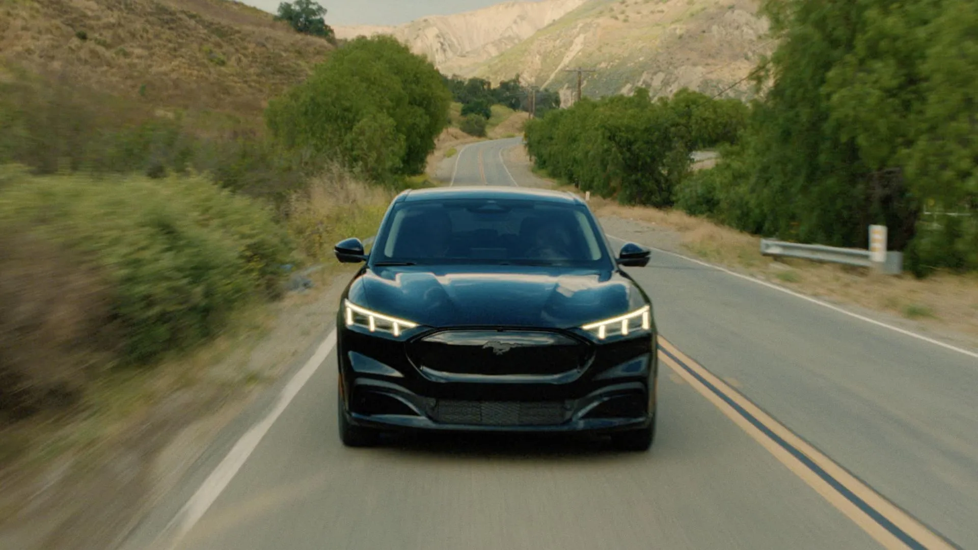 Ford Mustang Mach-E Select eAWD 2025 màu đen mạnh mẽ trên con đường quê, kết hợp phong cách cơ bắp với công nghệ xe điện.