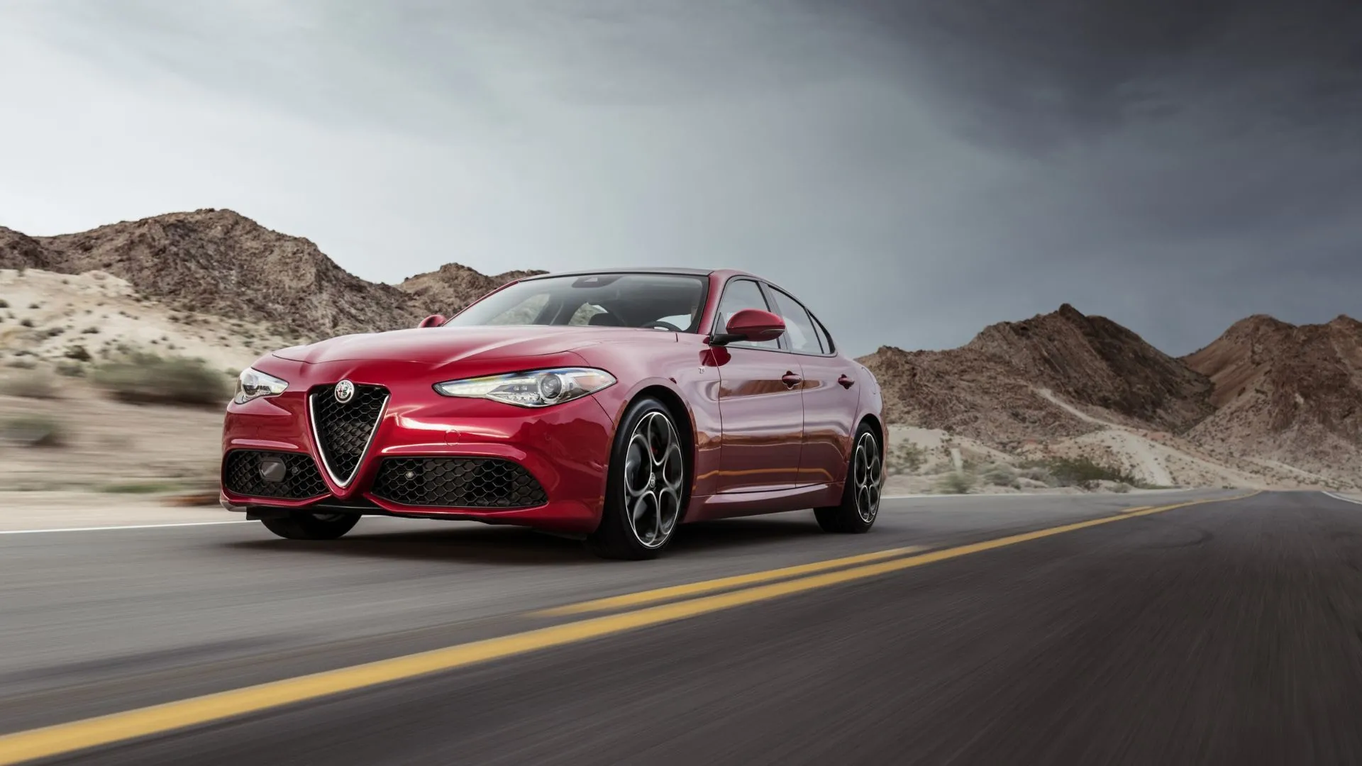 Góc 3/4 phía trước động của chiếc Alfa Romeo Giulia màu đỏ đời 2022 đang lái trên đường nông thôn với núi non làm nền.