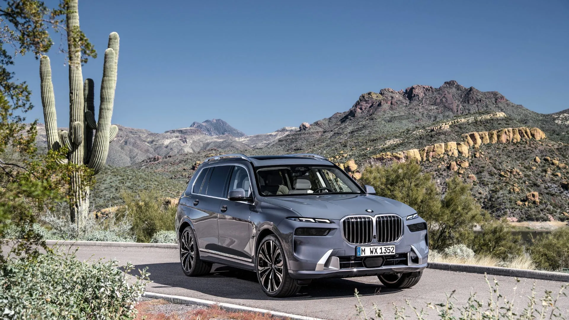 Góc ba phần tư phía trước của chiếc BMW X7 2022 màu xám đậu trên con đường ở sa mạc với xương rồng.