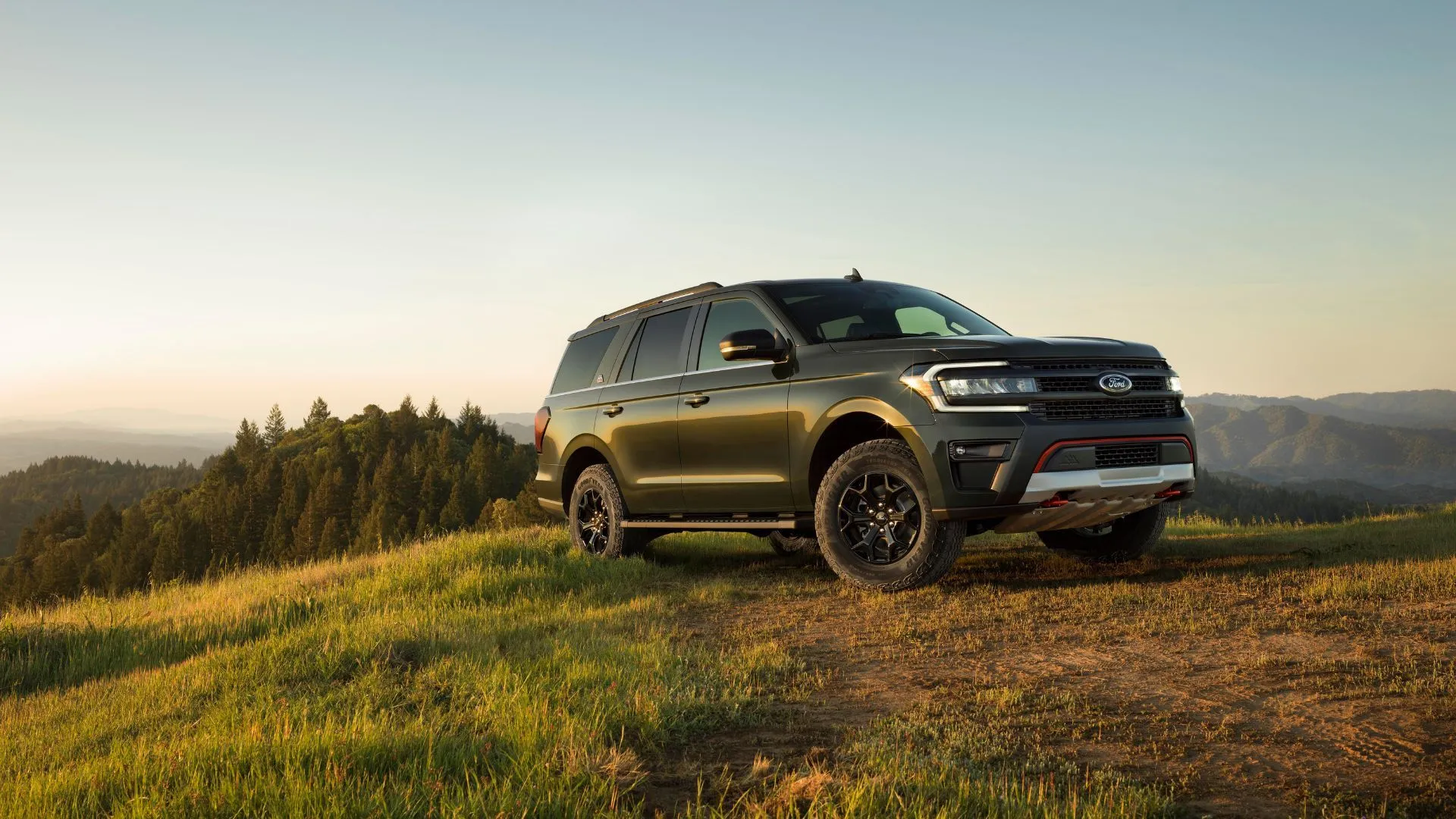 Góc ba phần tư phía trước của chiếc Ford Expedition 2023 màu xanh lá cây đậu trên bãi cỏ ở vùng nông thôn.