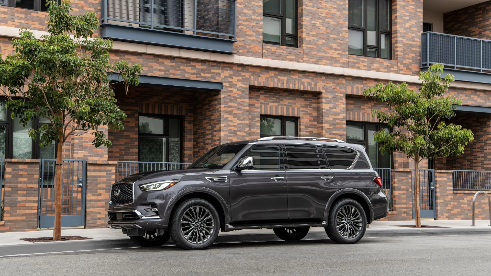 Góc ba phần tư phía trước của chiếc INFINITI QX80 2023 màu xám đậu bên ngoài một tòa nhà dân cư.