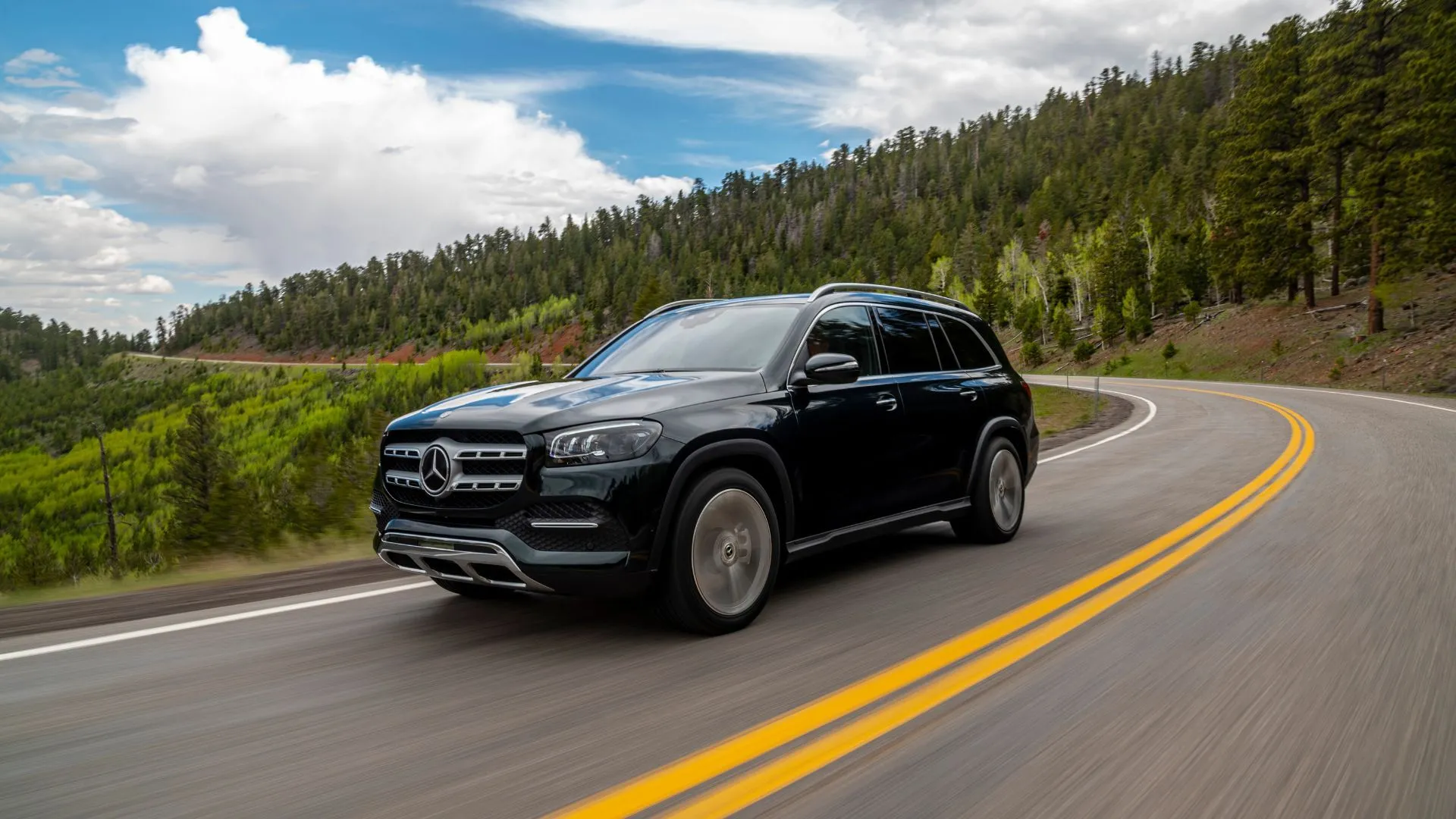 Góc ba phần tư phía trước của chiếc Mercedes-Benz GLS màu đen đang lái trên con đường nông thôn quanh co.