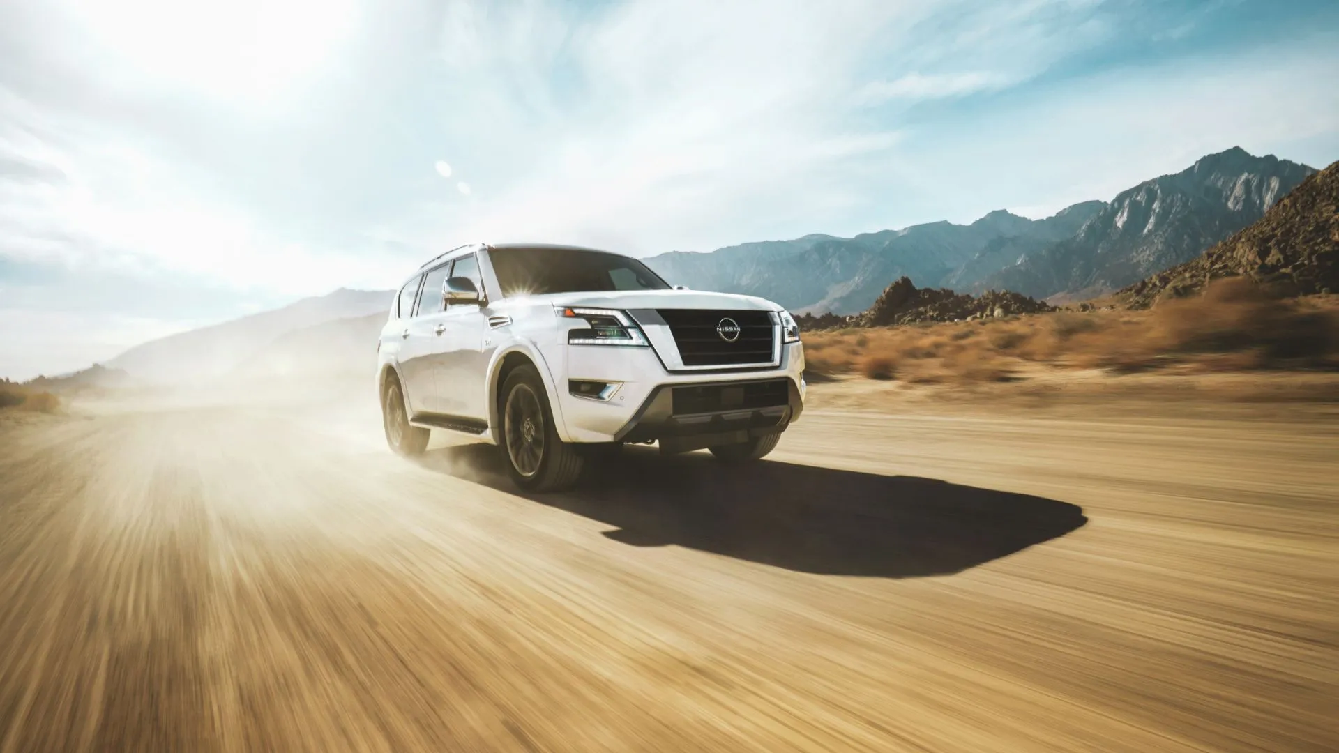 Góc ba phần tư phía trước của chiếc Nissan Armada 2022 màu trắng đang chạy off-road trên sa mạc.