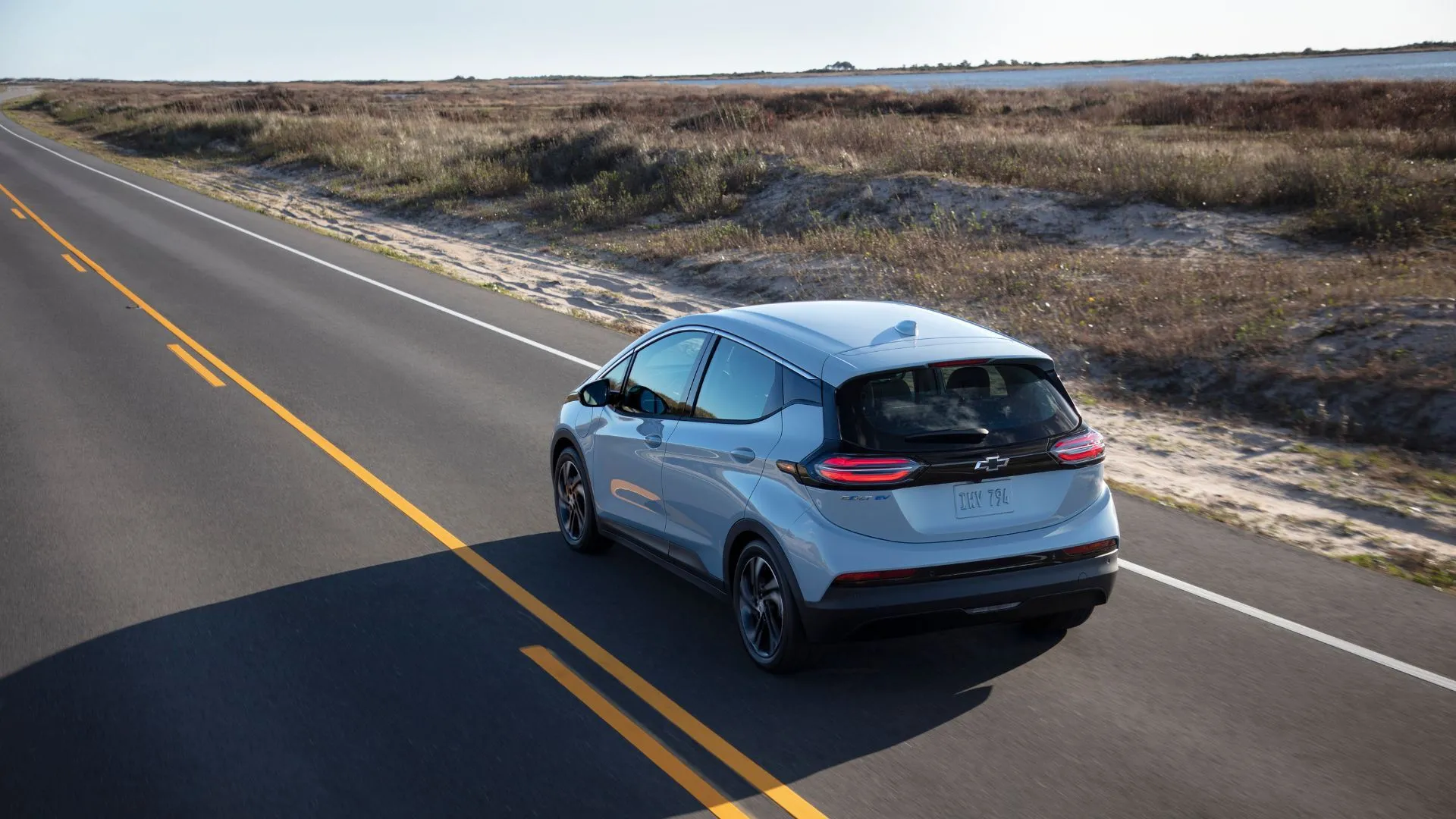 Góc nhìn 3/4 phía sau chiếc Chevrolet Bolt EV 2022 màu bạc đang di chuyển trên đường nông thôn, cho thấy thiết kế tổng thể của mẫu xe điện cũ này.