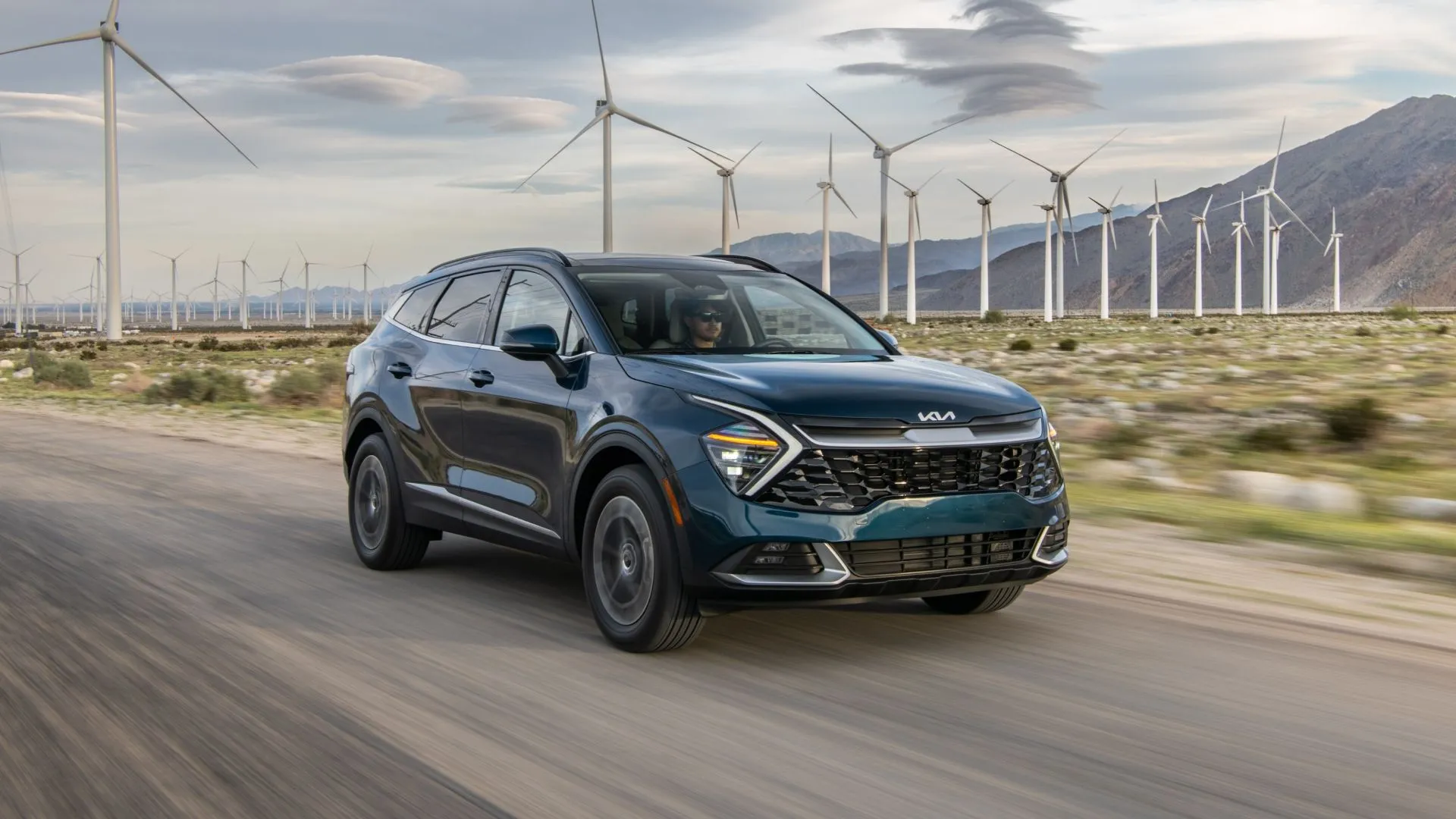 Góc trước của Kia Sportage Hybrid 2025 màu xanh ngọc đang di chuyển trên đường.