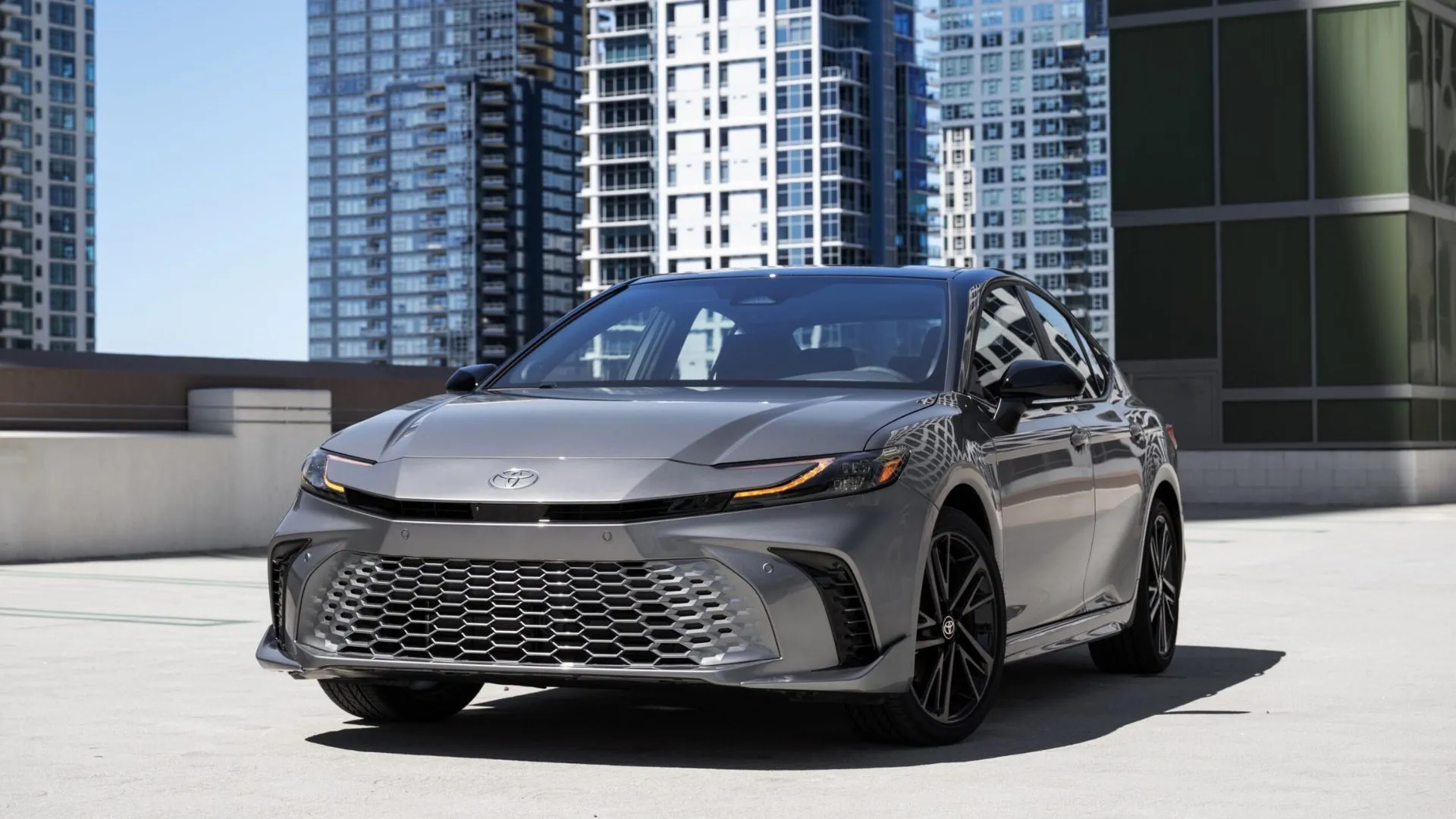 Hình ảnh cận cảnh chiếc Toyota Camry XSE Hybrid 2025 màu xám bạc, nổi bật trên nền các tòa nhà cao tầng, đại diện cho phiên bản AWD.