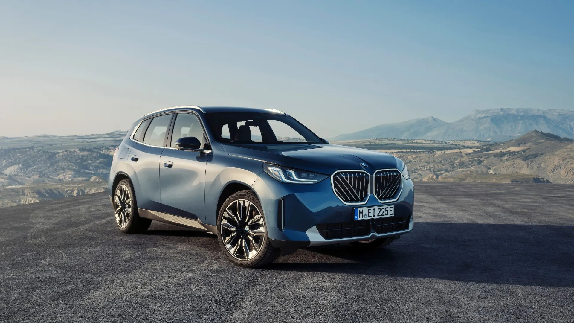 Hình ảnh góc 3/4 của BMW X3 30 xDrive 2025 màu xanh dương với phong cảnh núi non phía sau