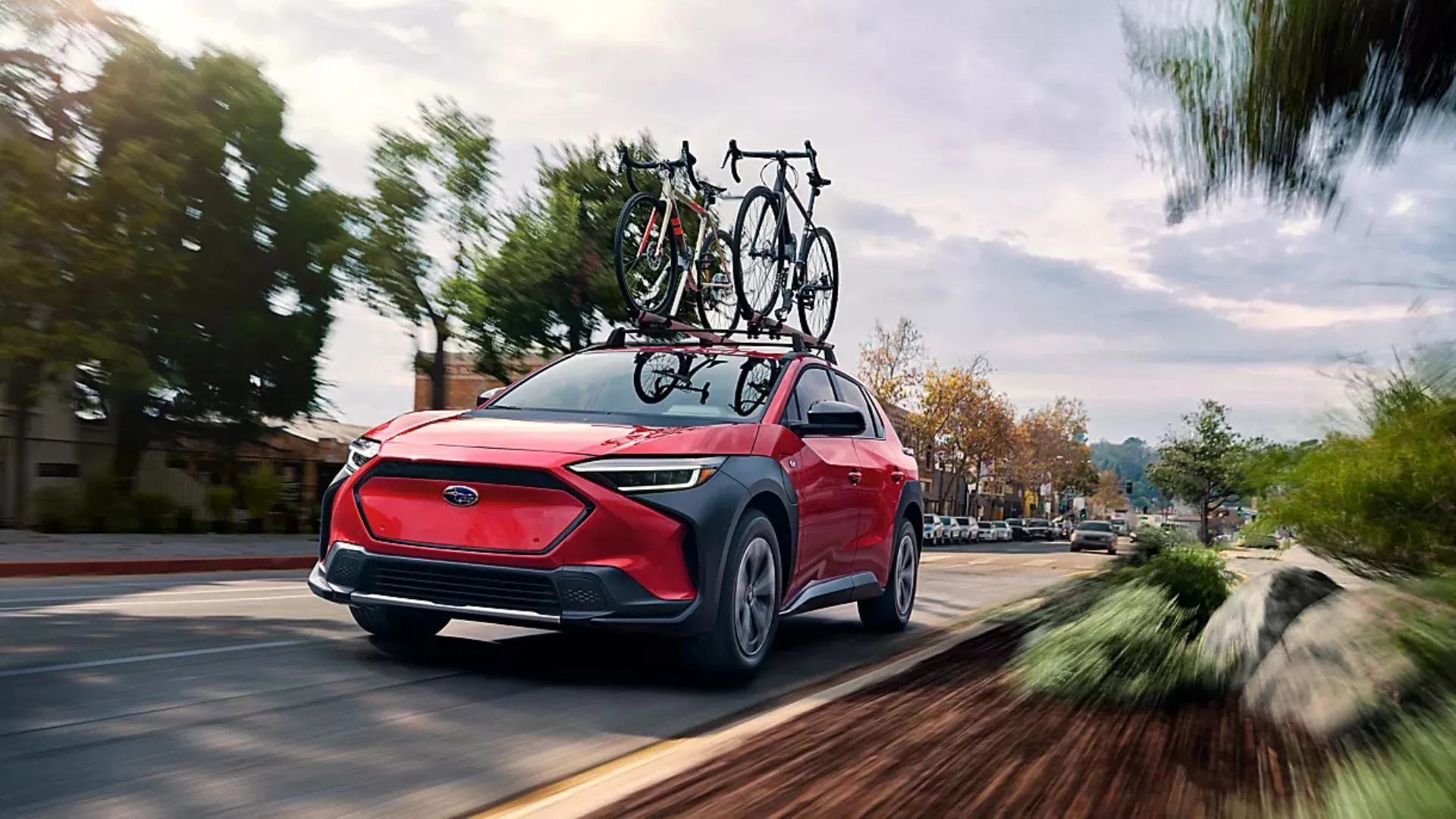 Hình ảnh mặt trước ba phần tư năng động của chiếc Subaru Solterra 2025 màu đỏ đang lái trên đường nông thôn, có gắn xe đạp trên nóc.