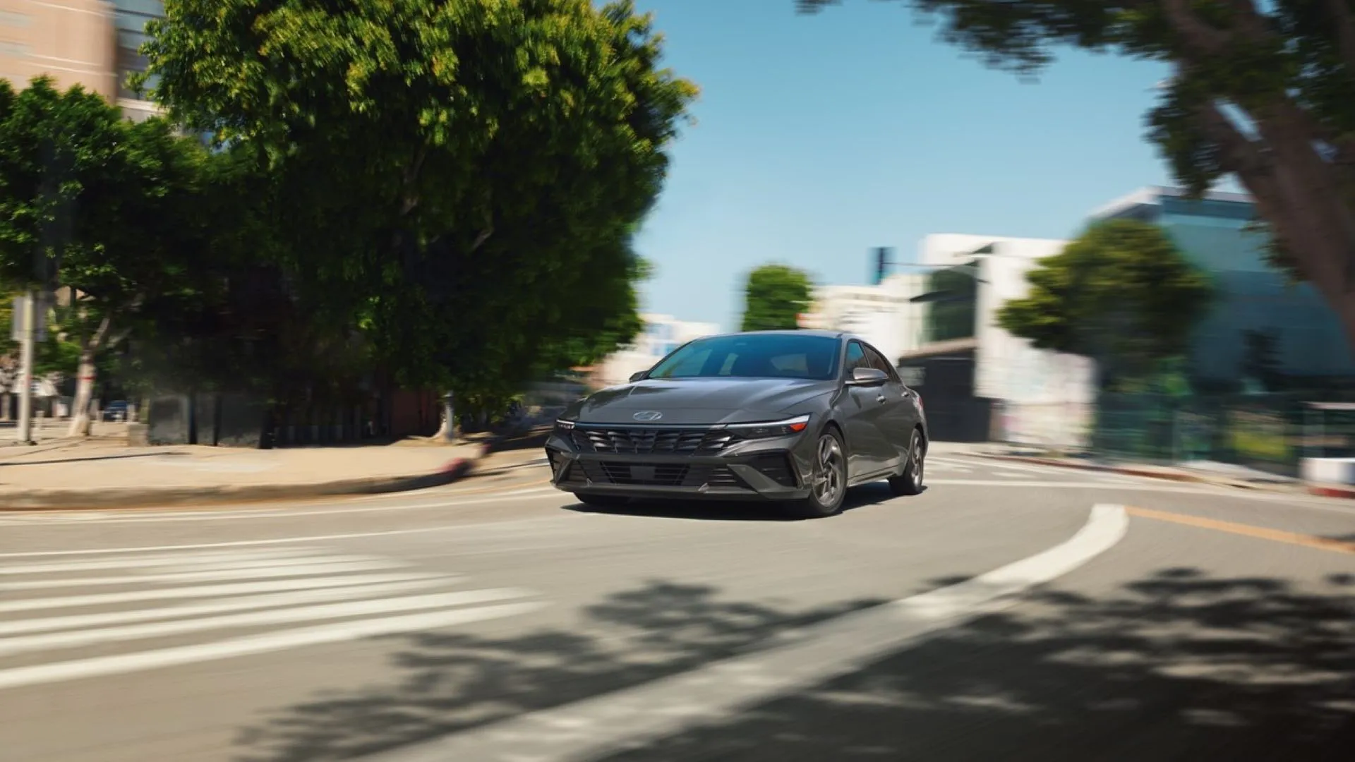 Hyundai Elantra Hybrid 2025 màu trắng bạc, góc 3/4 phía trước trên đường, thể hiện thiết kế năng động và hiệu quả.