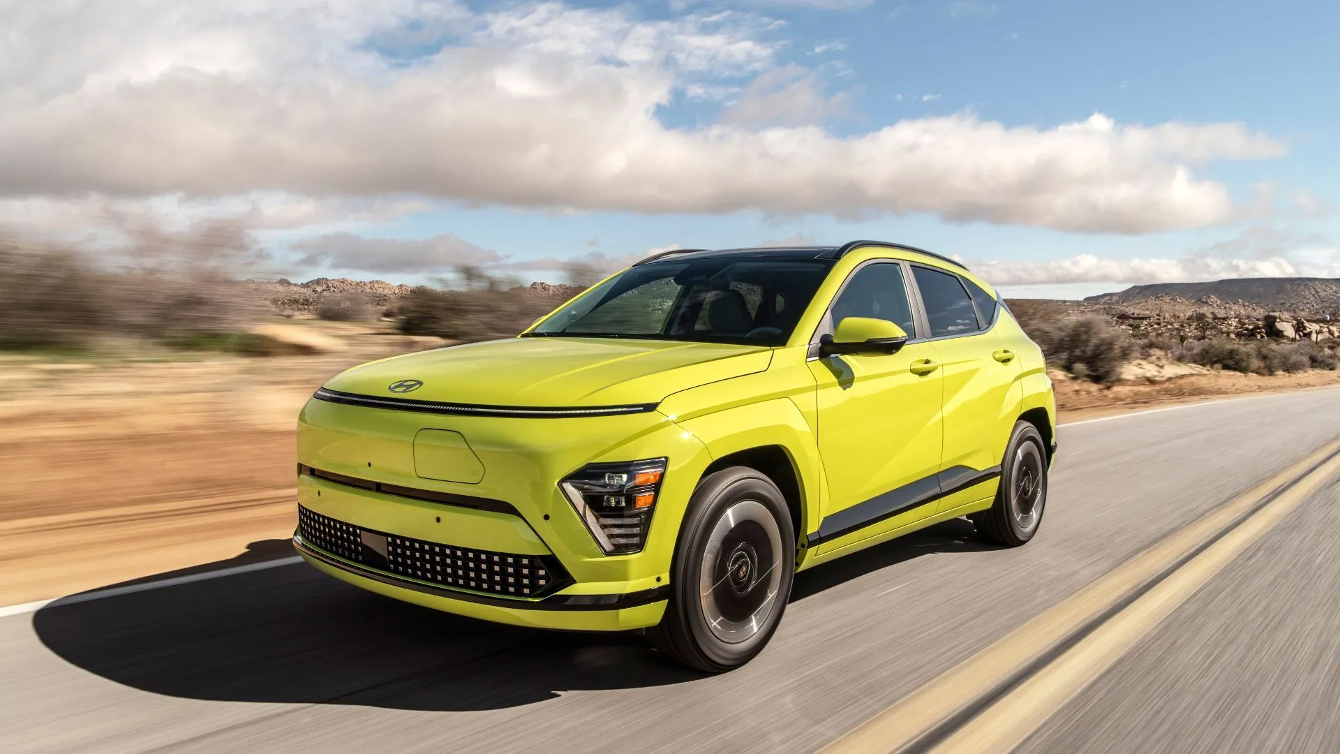 Hyundai Kona Electric 2025 màu vàng nổi bật, đang di chuyển trên đường nông thôn, kết hợp phong cách và khả năng vận hành điện.