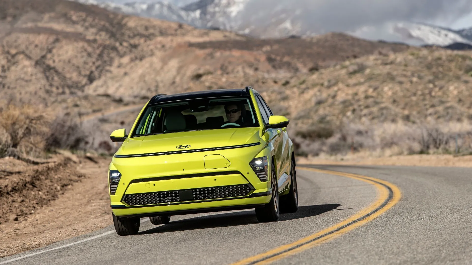 Hyundai Kona Electric 2025 màu vàng rực rỡ đang di chuyển trên con đường quanh co, thể hiện sự độc đáo và giá trị của mẫu crossover điện.