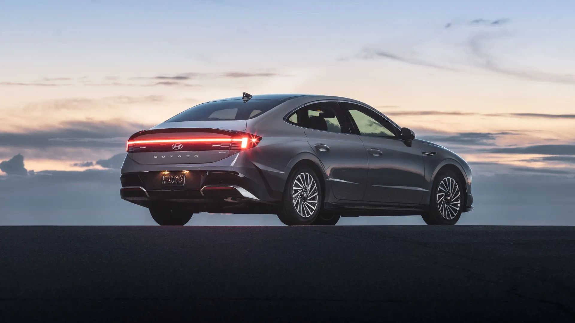 Hyundai Sonata Hybrid Limited 2025 màu xám bạc nhìn từ góc 3/4 phía sau trong ánh hoàng hôn, toát lên vẻ sang trọng.