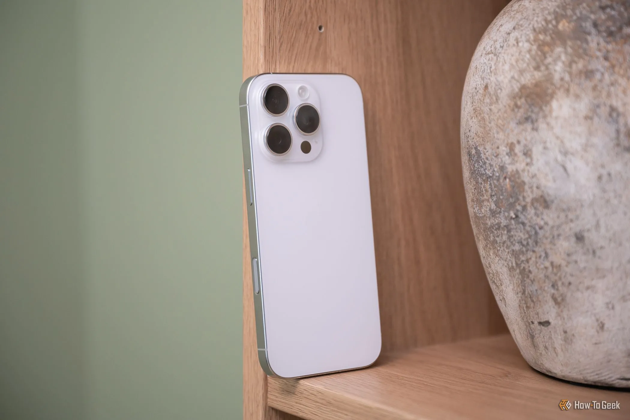 iPhone 16 Pro màu xanh titan đặt trên giá sách, hiển thị nút điều khiển camera mới, nâng cao trải nghiệm chụp ảnh trên iPhone.