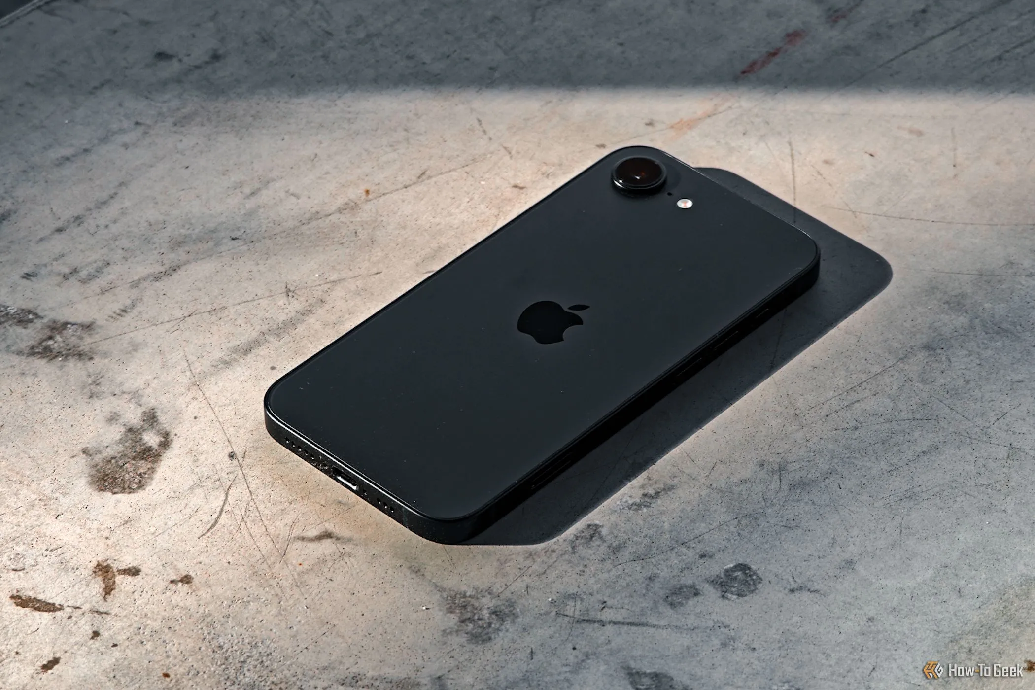 iPhone 16e nằm úp trên nền bê tông, thể hiện độ bền và thiết kế tối giản.