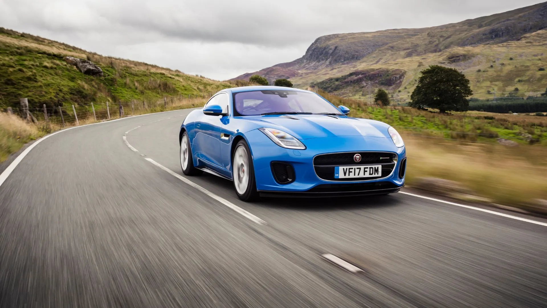 Jaguar F-TYPE 2017 màu xanh lam đang di chuyển trên con đường quanh co ở vùng nông thôn Anh, toát lên vẻ đẹp thể thao và mạnh mẽ