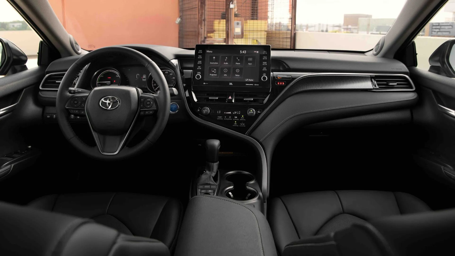 Khoang nội thất màu đen của Toyota Camry Hybrid 2022 với vô lăng, bảng điều khiển và màn hình thông tin giải trí trung tâm, thể hiện sự tiện nghi và công nghệ bên trong xe.