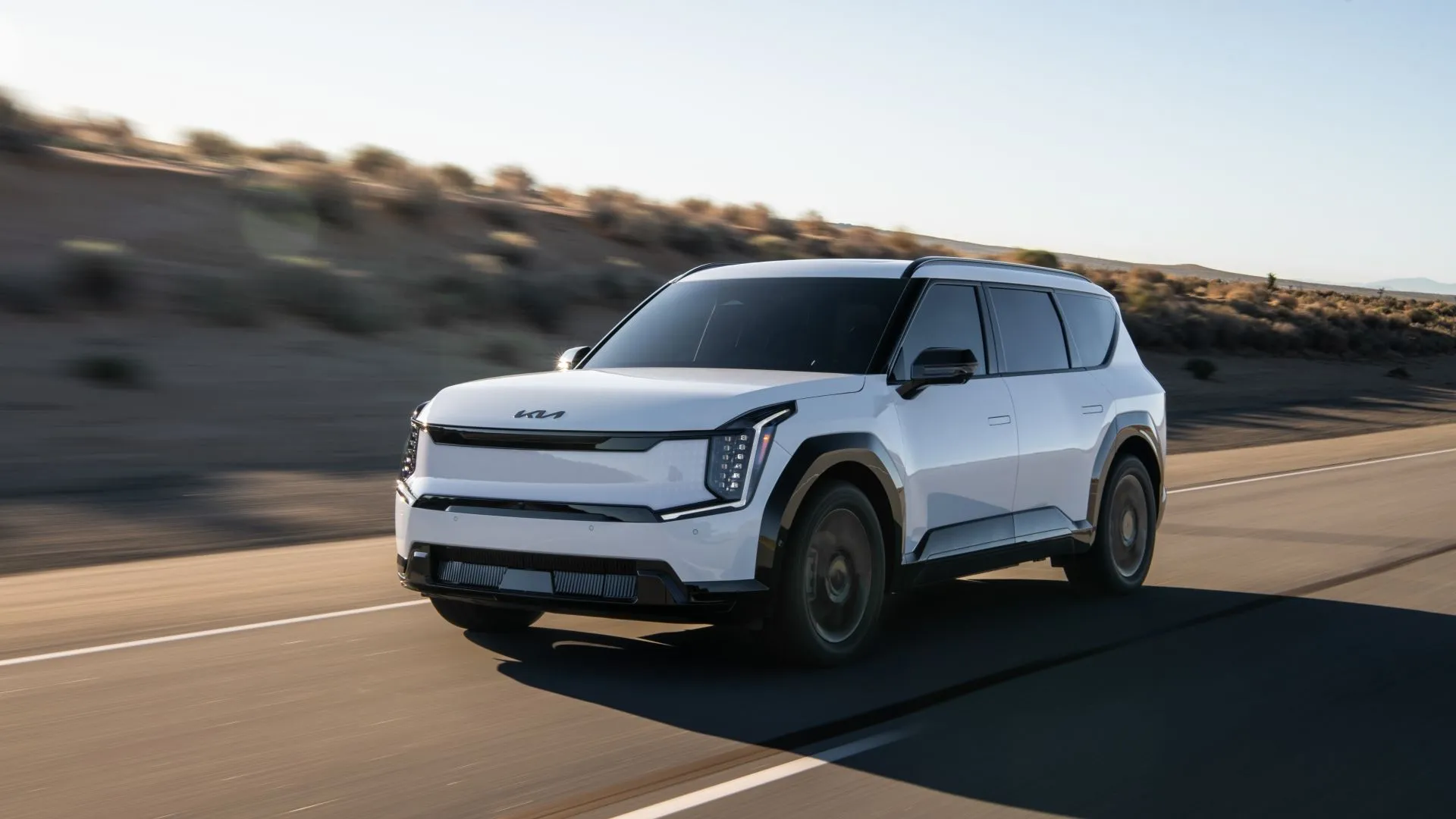 Kia EV9 2025 màu xanh đậm với kiểu dáng SUV hộp hiện đại, đang di chuyển trên đường.