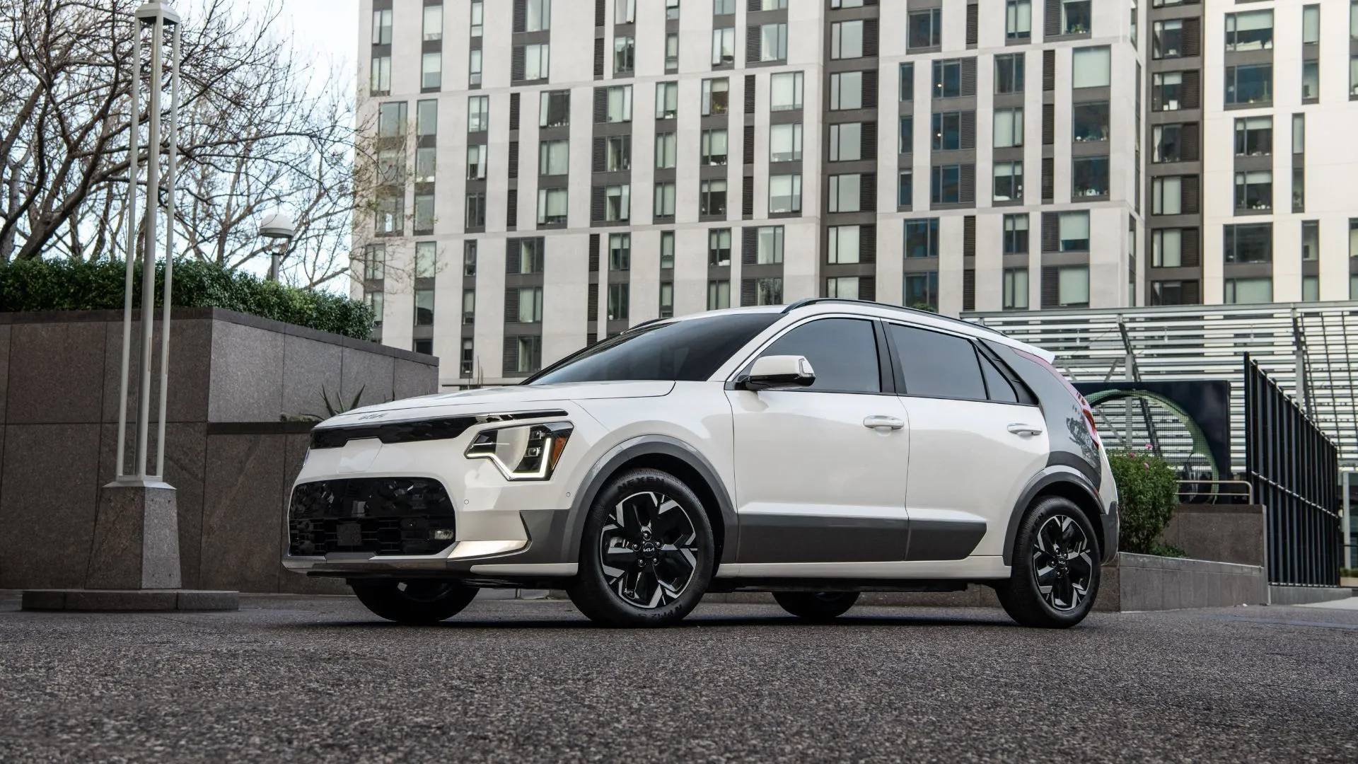 Kia Niro EV 2025 màu trắng đỗ trước tòa nhà lớn, thể hiện sự thực dụng, dễ lái và quãng đường di chuyển tốt cho người dùng mới.