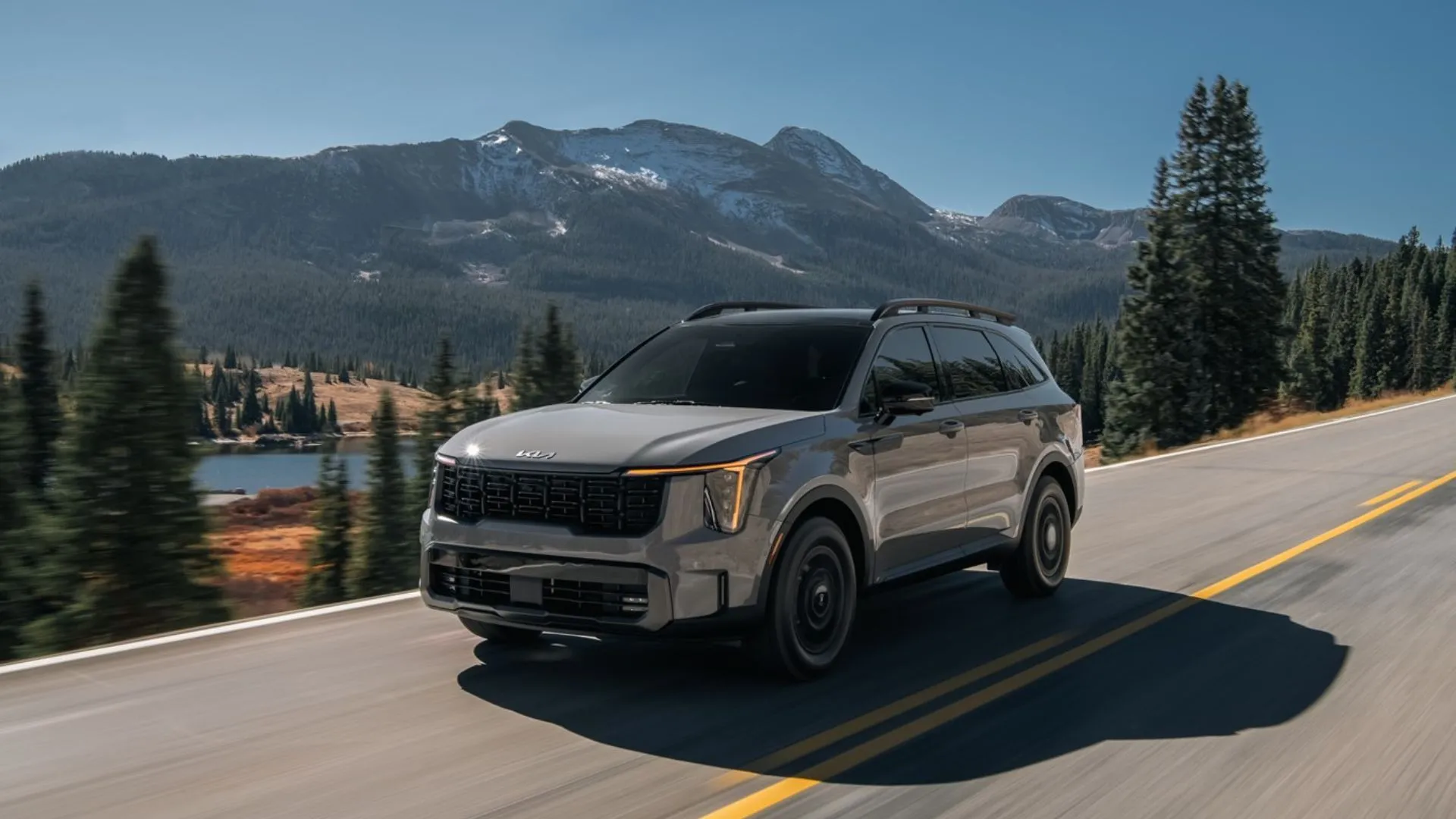 Kia Sorento Hybrid 2025 màu xám, góc 3/4 phía trước, trên đường nông thôn có núi
