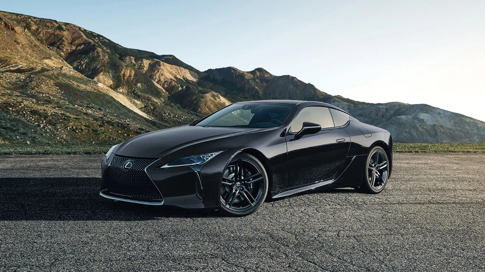 Lexus LC 500 2025 màu đen đậu trên sỏi với phong cảnh núi non hùng vĩ phía sau