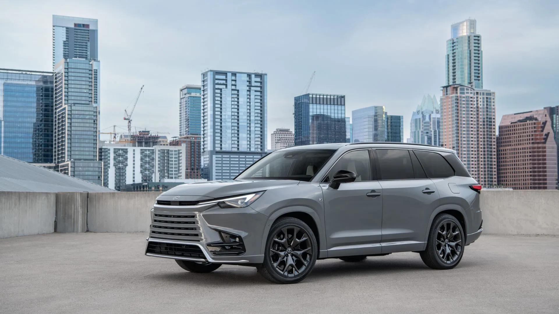 Lexus TX 500h F Sport Performance 2024 màu xám đỗ trên sân thượng với phong cảnh thành phố và những tòa nhà chọc trời phía sau