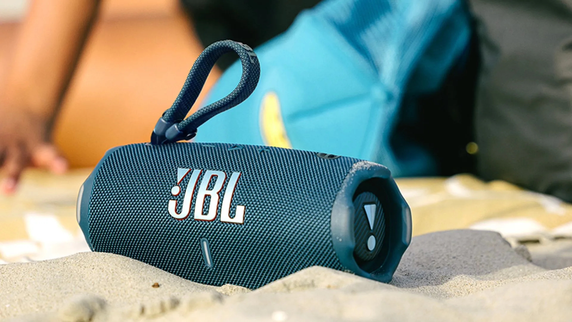 Loa di động JBL Charge 6 màu xanh dương trên cát, phù hợp cho các chuyến phiêu lưu mùa hè.