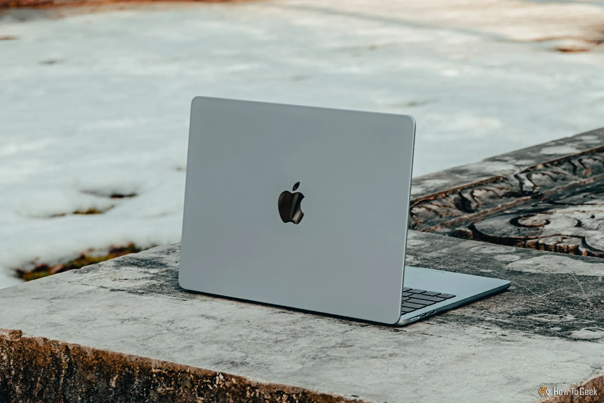 MacBook Air M4 màu xanh lam nghiêng đặt trên ghế đá bê tông, thể hiện thiết kế mỏng nhẹ của laptop