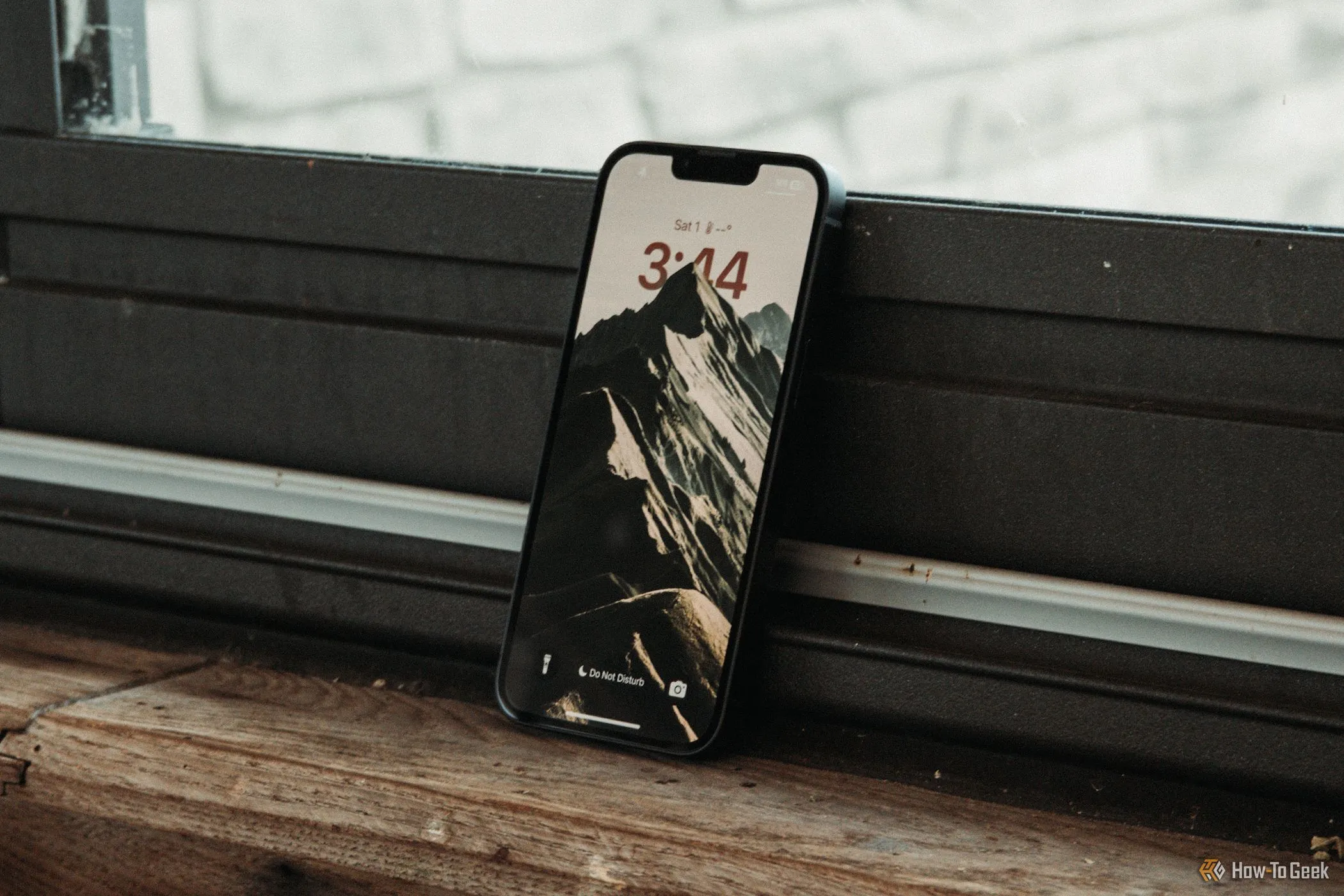 Màn hình khóa của iPhone 16e hiển thị giờ và widget, đặt nghiêng trên bệ cửa sổ, phản ánh giao diện người dùng iOS.