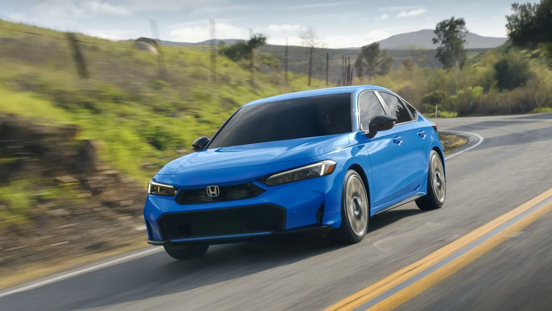 Mẫu Honda Civic Hatchback Sport Touring Hybrid 2025 màu đen, góc 3/4 phía trước, trên đường phố.