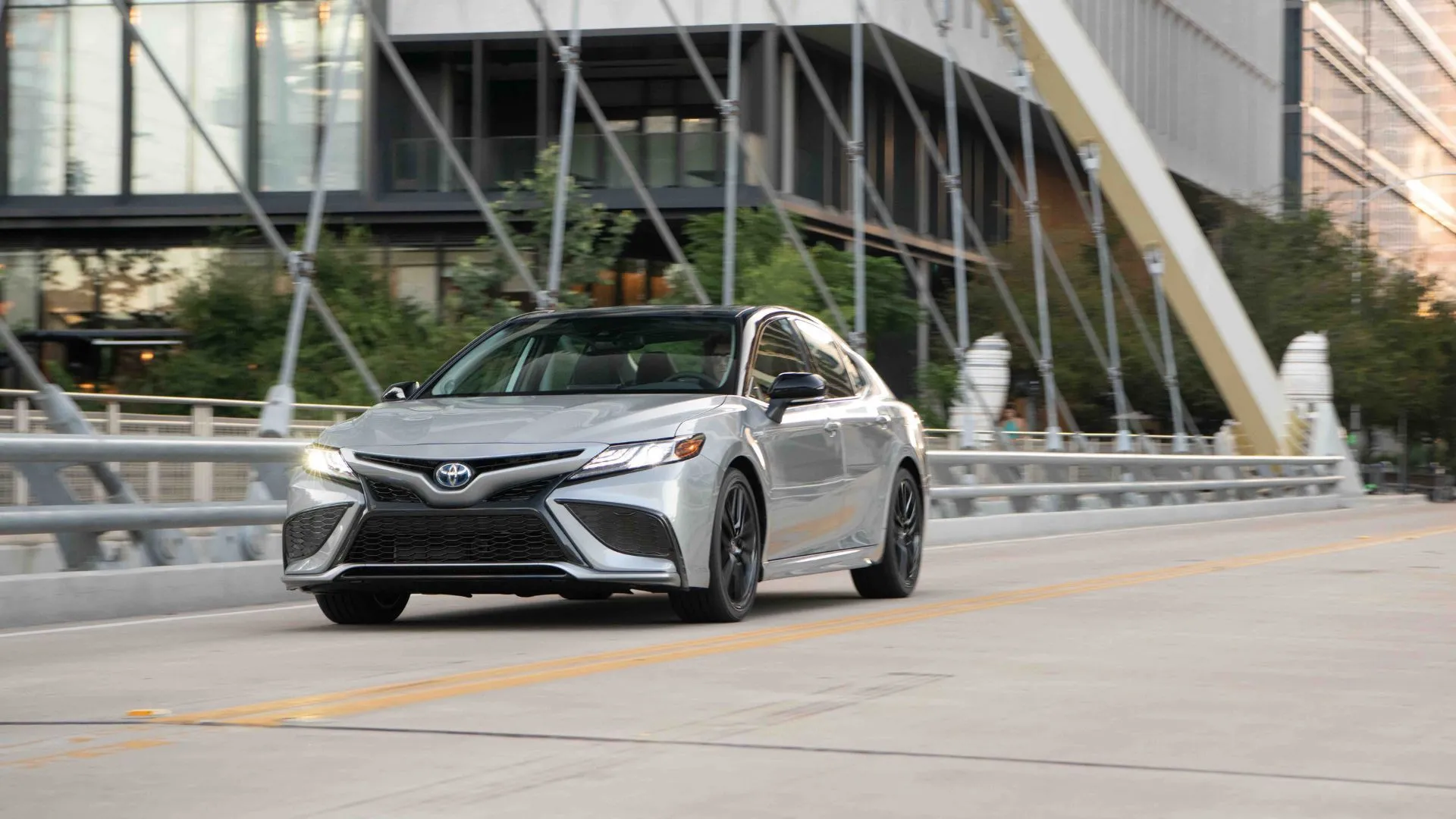 Mẫu xe Toyota Camry Hybrid 2022 màu bạc-đen đang di chuyển trong thành phố, đại diện cho dòng xe hybrid truyền thống