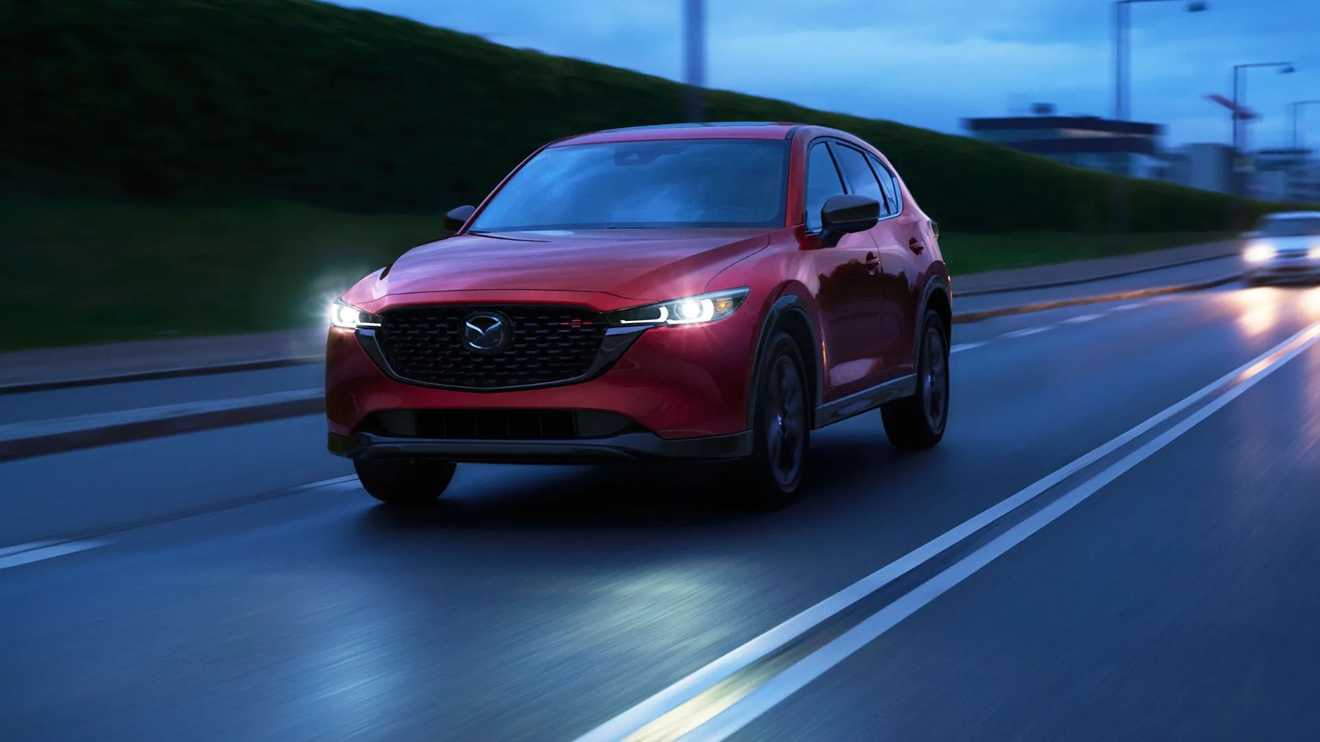 Mazda CX-5 2025 màu đỏ đô lái qua thành phố vào ban đêm.