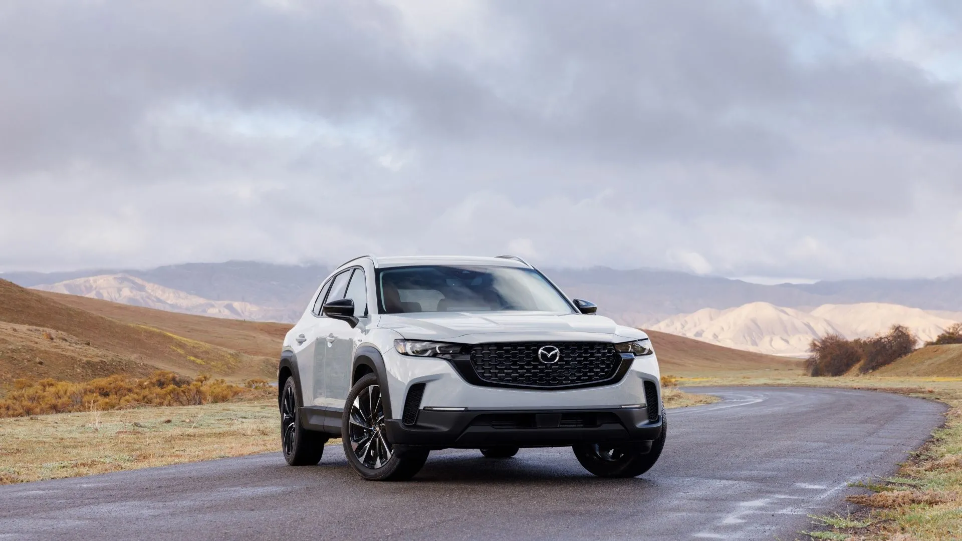 Mazda CX-50 Hybrid 2025 màu xám, góc 3/4 phía trước, trên con đường núi, kết hợp hiệu suất off-road với công nghệ hybrid tiết kiệm nhiên liệu.