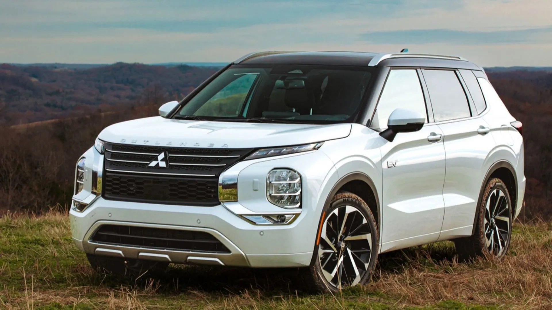 Mitsubishi Outlander PHEV 2025 màu trắng bạc đậu giữa khung cảnh thiên nhiên.