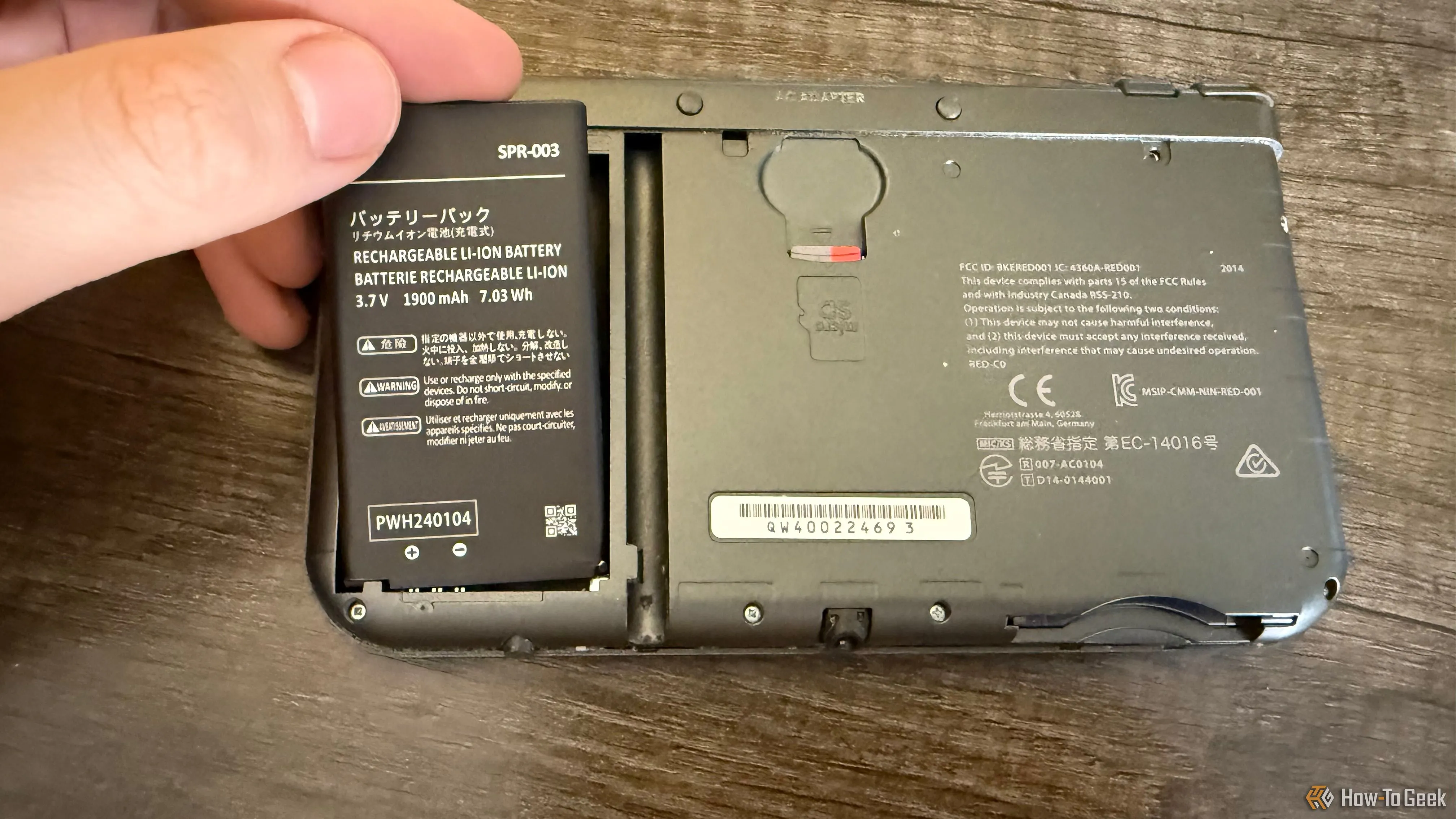 Một bàn tay đang nhẹ nhàng đặt viên pin thay thế vào khay pin của máy New Nintendo 3DS XL, đảm bảo các chân tiếp xúc khớp.