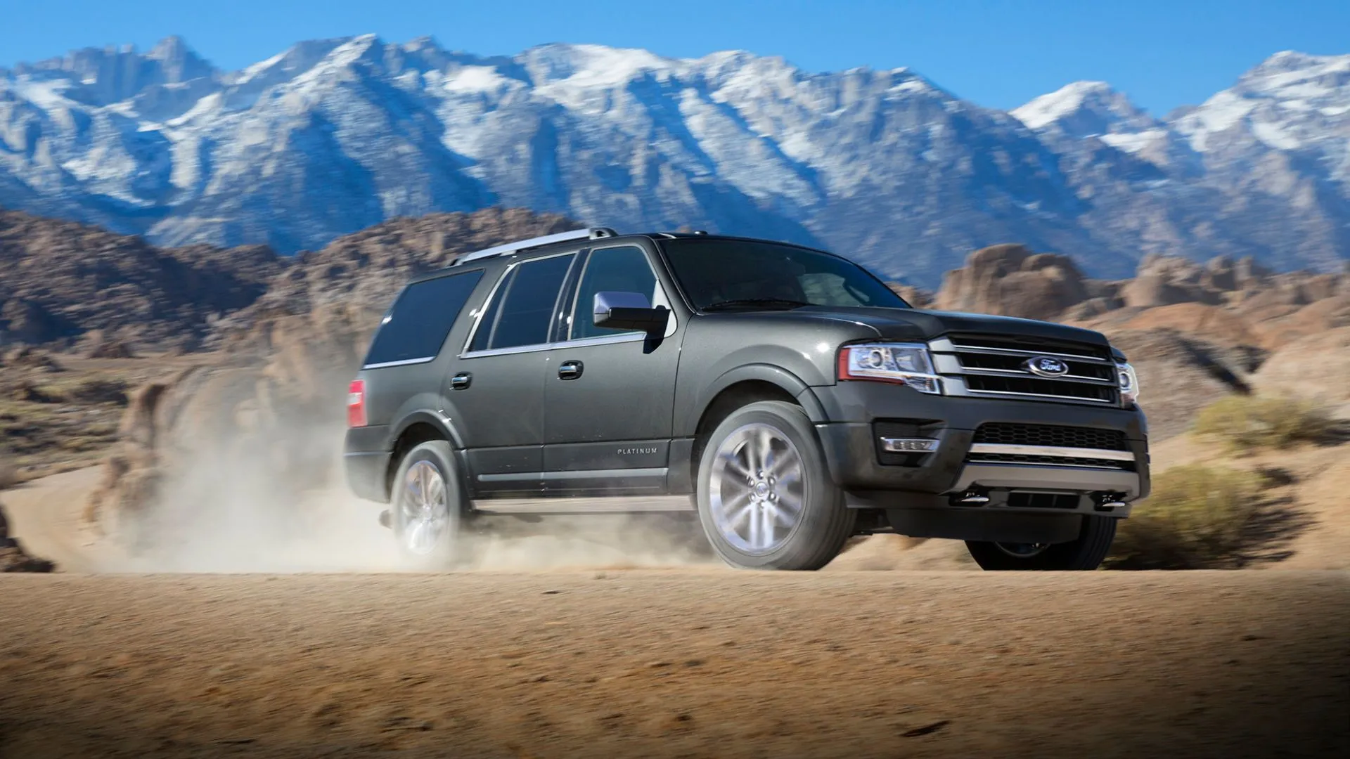 Một chiếc Ford Expedition 2017 màu xám đang vượt địa hình cát, với những ngọn núi phủ tuyết phía sau, minh họa khả năng off-road của SUV Ford.
