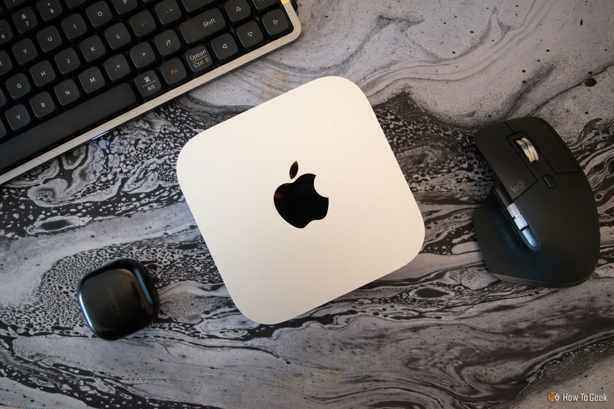 Một chiếc Mac Mini M4 đặt trên bàn làm việc, xung quanh là các thiết bị ngoại vi của PC.