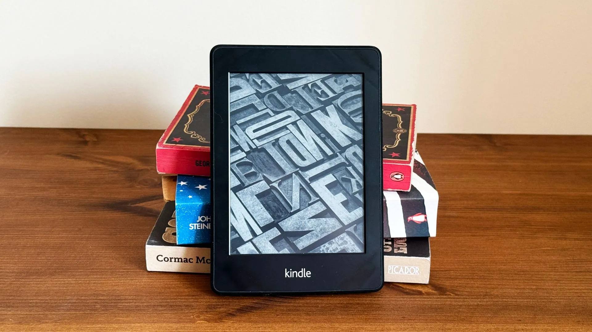 Một chồng sách giấy với một chiếc máy đọc sách Kindle đặt phía trước, tạo nên sự tương phản giữa công nghệ và truyền thống