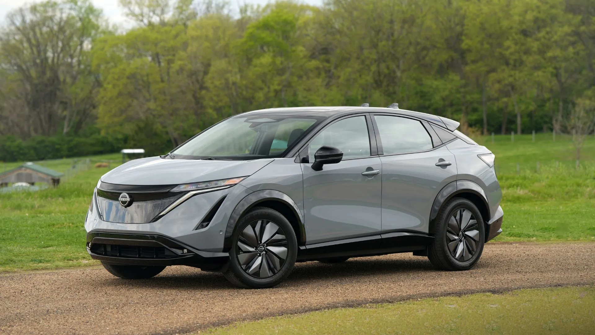 Nissan Ariya 2025 màu xám bạc đậu trên đường sỏi, với cảnh quan tự nhiên phía sau, toát lên vẻ sang trọng và tinh tế.