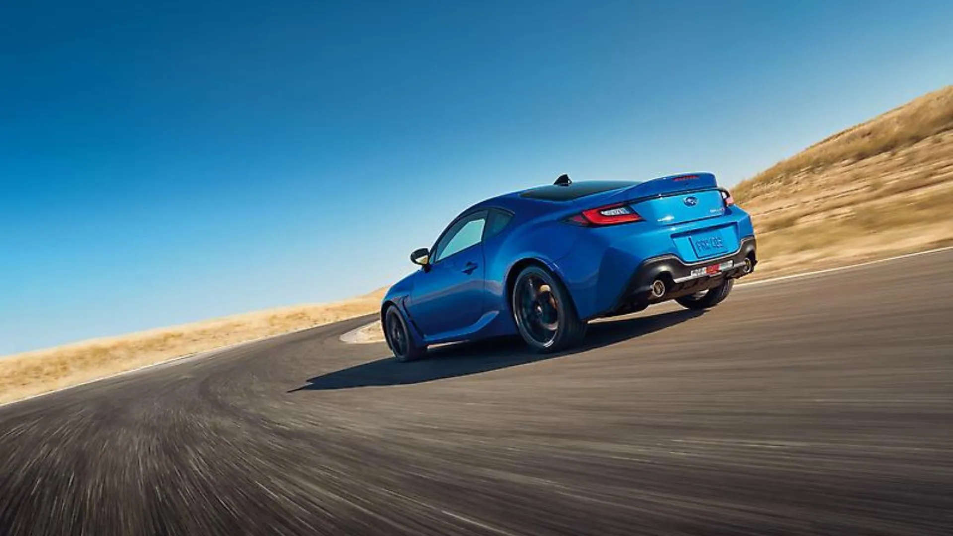 Subaru BRZ 2024 tS màu xanh năng động đang ôm cua trên con đường nông thôn với phong cảnh núi non hùng vĩ phía sau